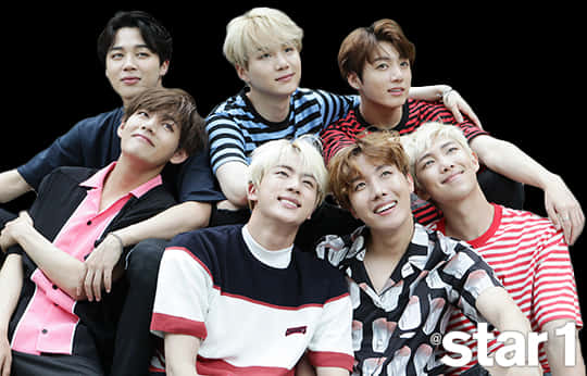 BTS 桌布 壁紙 — 七位身穿彩色條紋襯衫的年輕男性在黑色背景前緊密地擺姿勢，帶著自信的笑容。