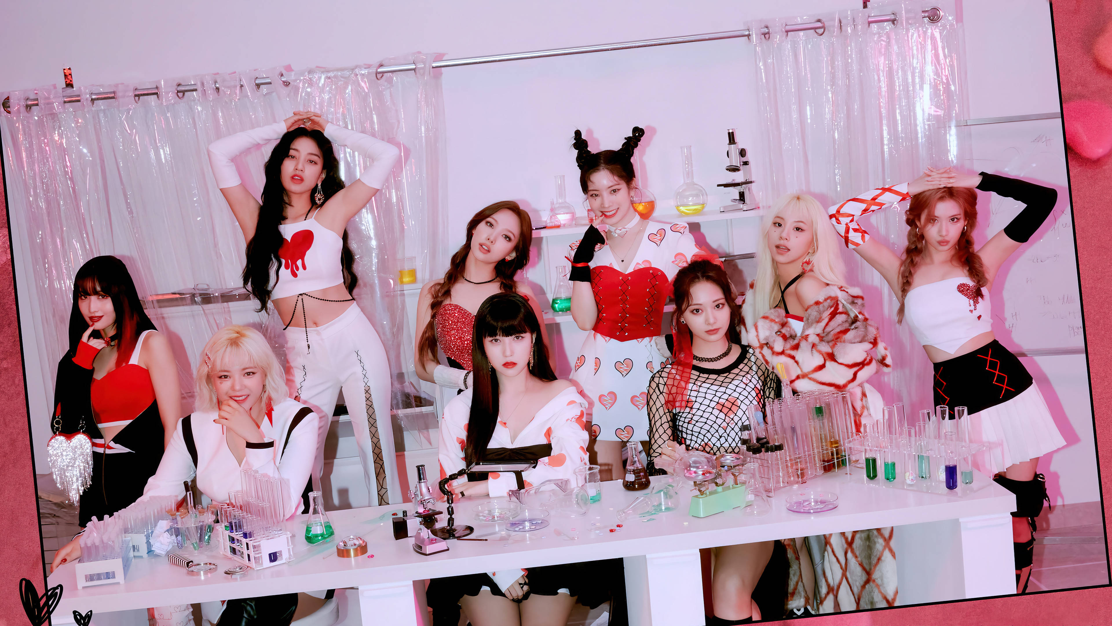 Kpop Aesthetic 桌布 壁紙 — 七位身穿心形主題服裝的女性自信地圍繞著一張裝滿彩色試管和科學道具的實驗桌擺姿勢。