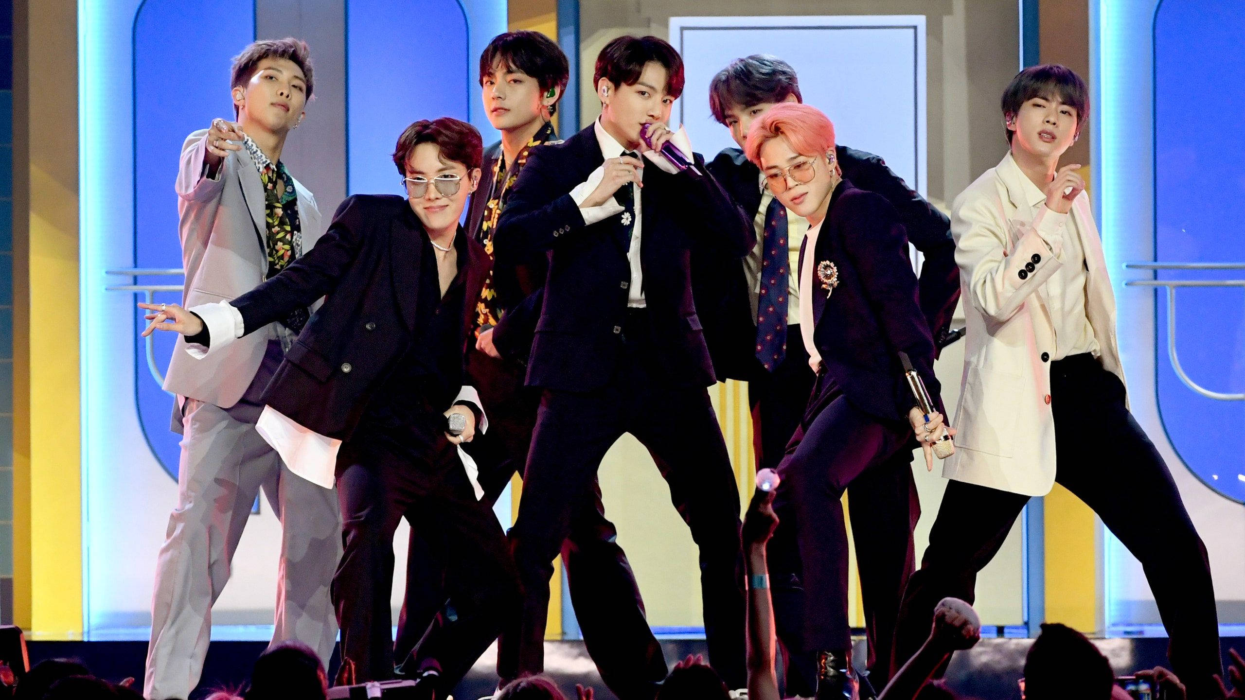 BTS 2021 桌布 壁紙 — 七位身穿時尚西裝的男K-pop偶像在燈光璀璨的舞台上充滿活力地表演，背景為藍色和黃色。