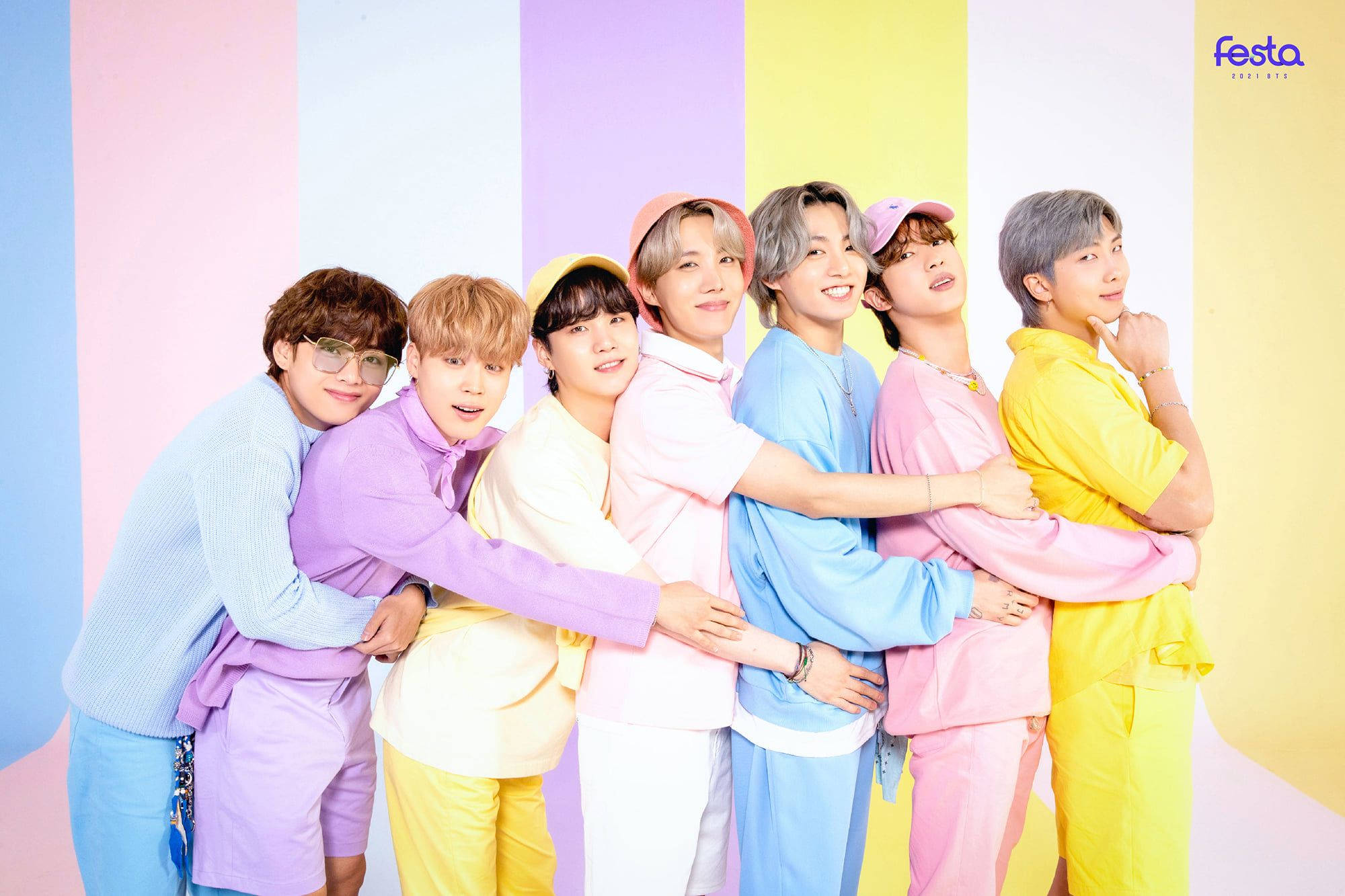 BTS 2021 桌布 壁紙 — 七位身穿柔和色調服裝的年輕男子，在色彩繽紛的條紋背景前擠在一起，表情愉快。