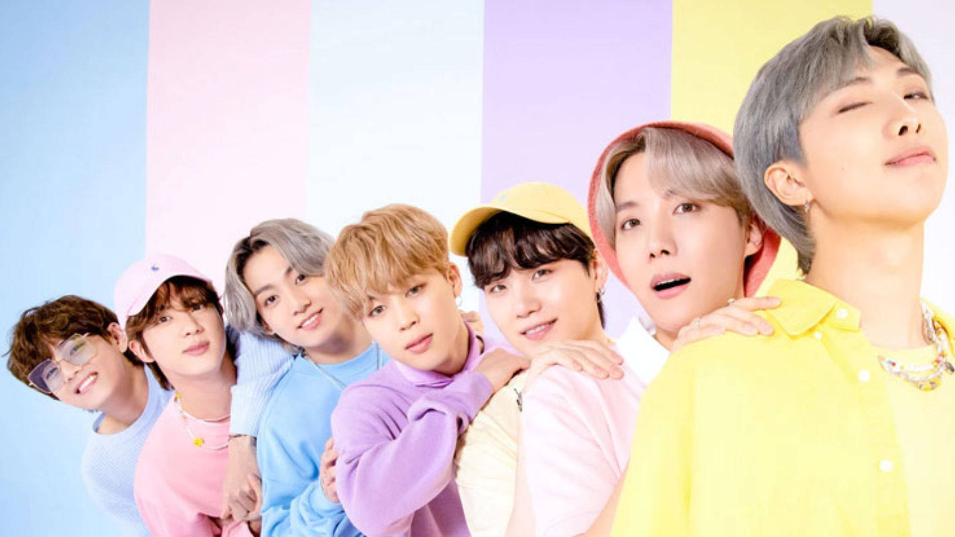 BTS 桌布 壁紙 — 七位身穿柔和色調服裝的年輕男性在充滿活力的條紋背景前緊密擺姿勢。