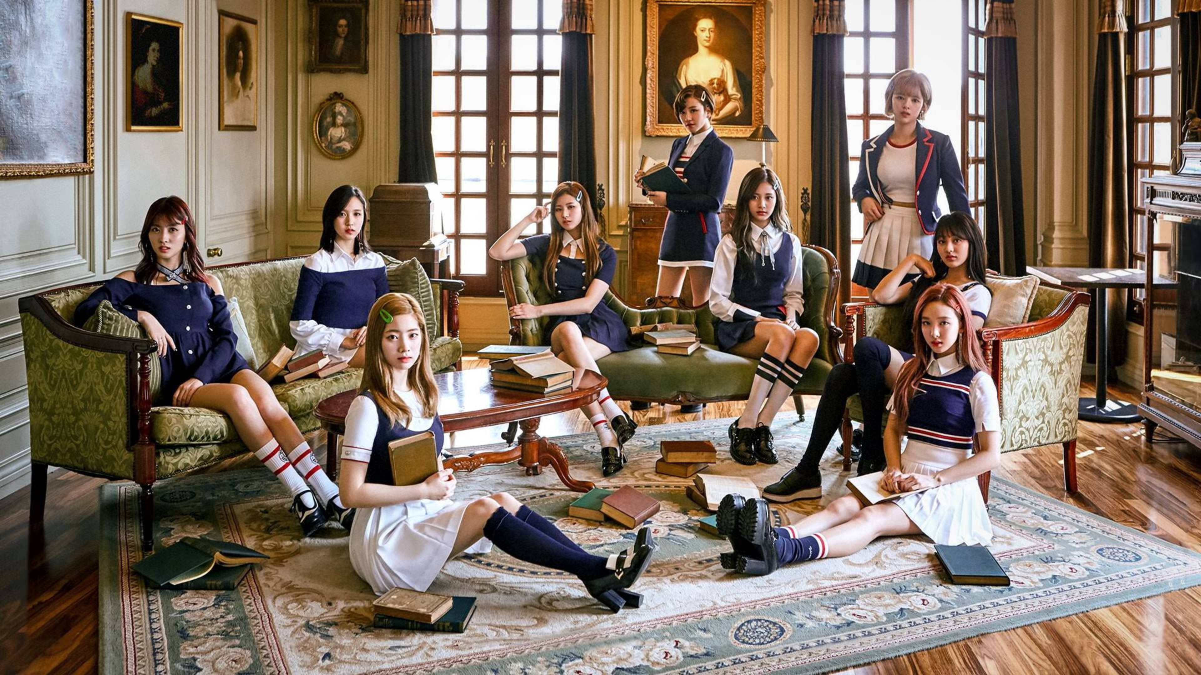 Kpop Aesthetic 桌布 壁紙 — 七位身穿校服的年輕女性在一個宏偉、陽光普照的維多利亞式書房裡優雅地擺姿勢，書房裡擺滿了書籍和古董家具。