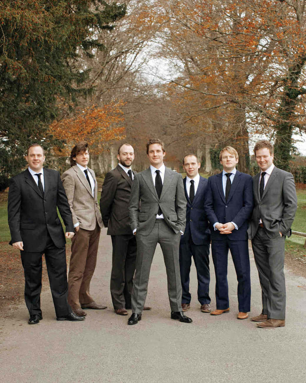 Groomsmen 桌布 壁紙 — 七位身穿正式西裝的男士一起站在一條鋪砌的小徑上，周圍是帶有橙色和綠色葉子的秋樹。