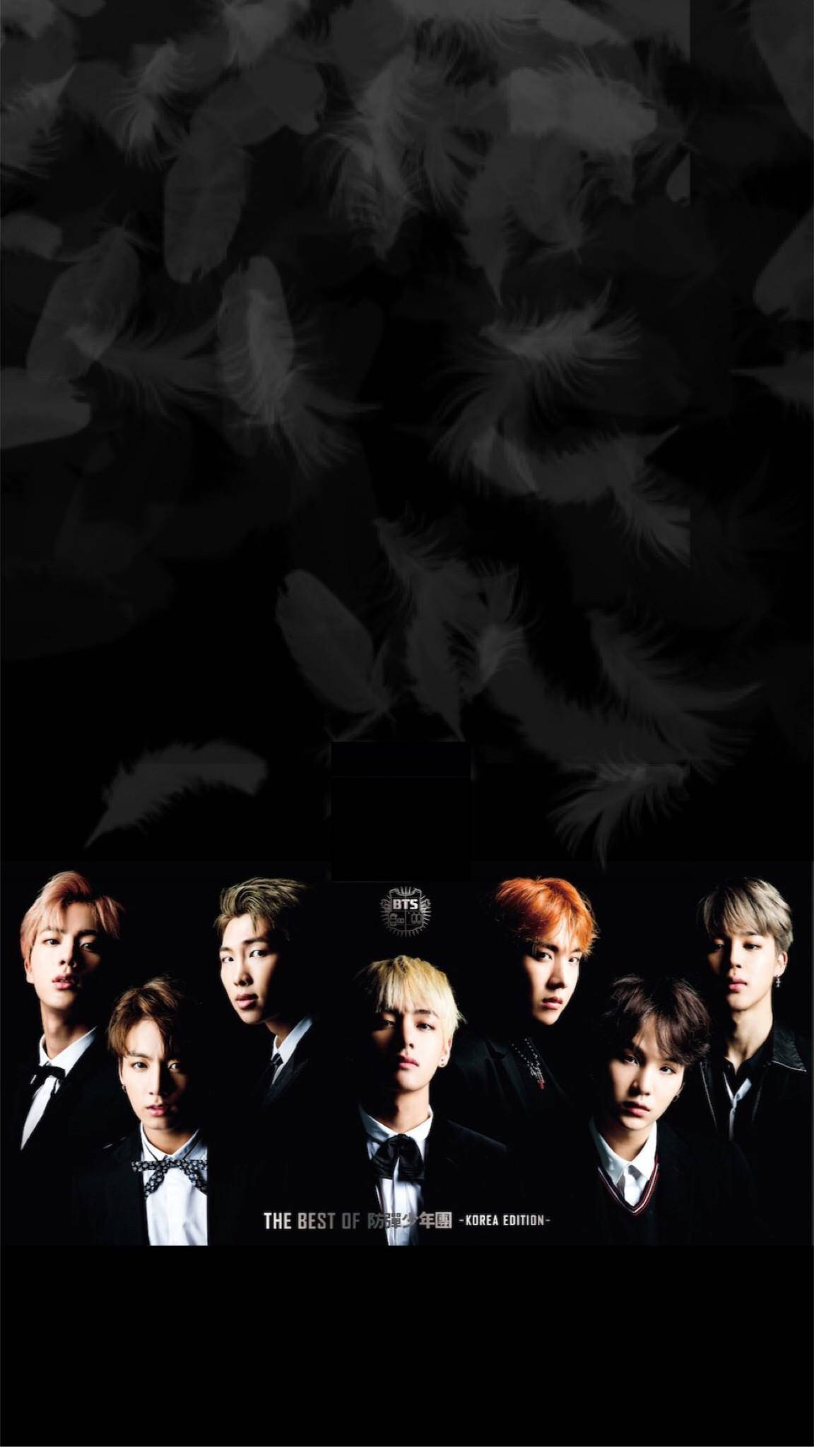 BTS 黑色 桌布 壁紙 — 七位身穿正式黑色西裝的男士站在一個有漂浮羽毛和戲劇性燈光的黑暗背景前。