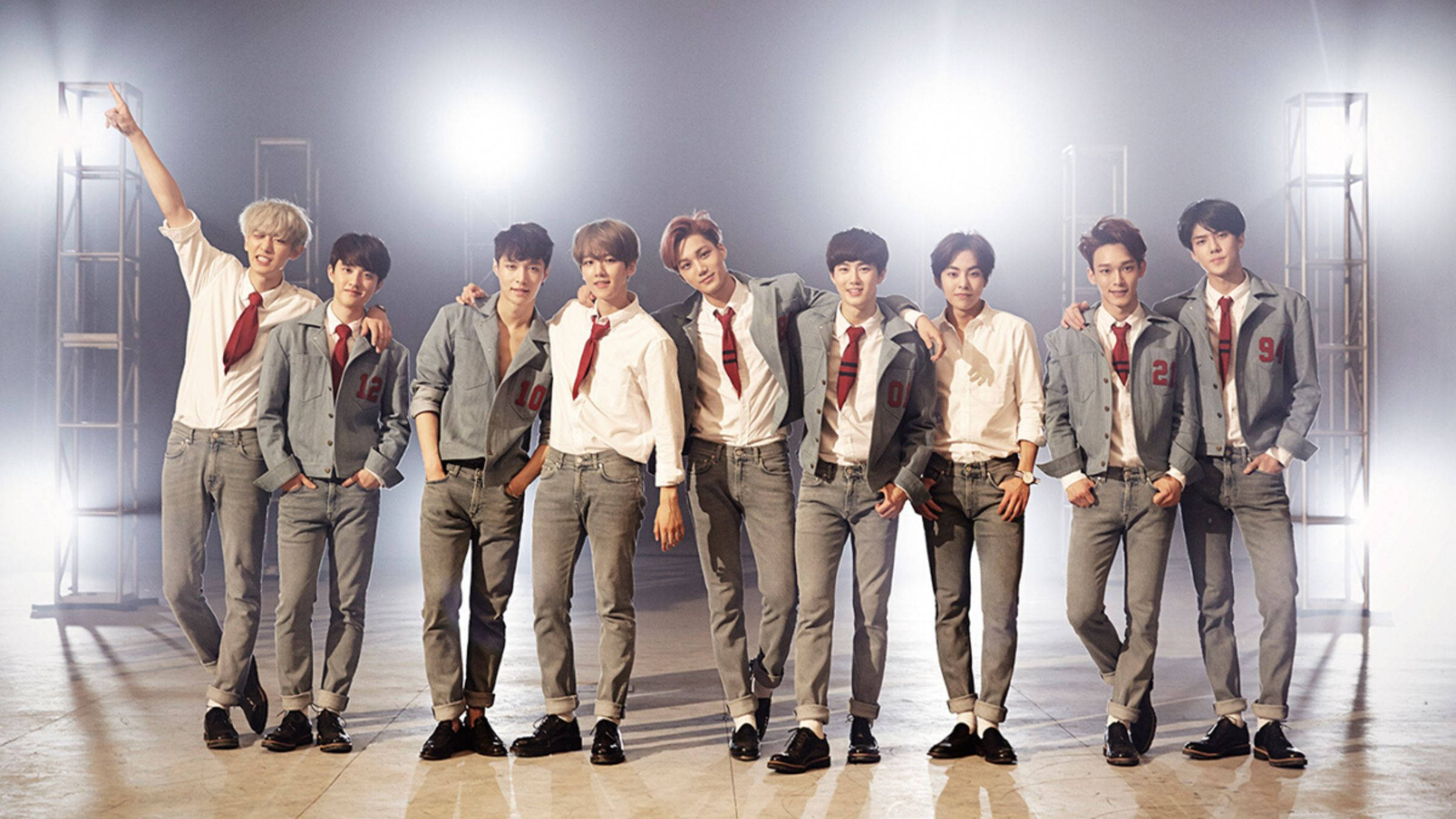 EXO 桌布 壁紙 — 七位身穿灰色外套和紅色領帶的年輕男子在明亮的攝影棚燈光下自信地擺姿勢，背景有霧氣。