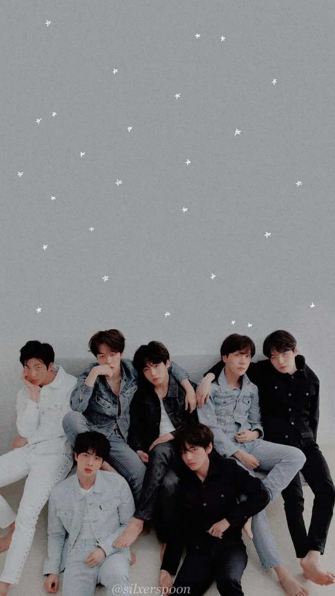 BTS 桌布 壁紙 — 七位身穿牛仔布和深色服裝的年輕男子，在點綴著白色星星的灰色天空下，隨意地坐在淺色地板上。
