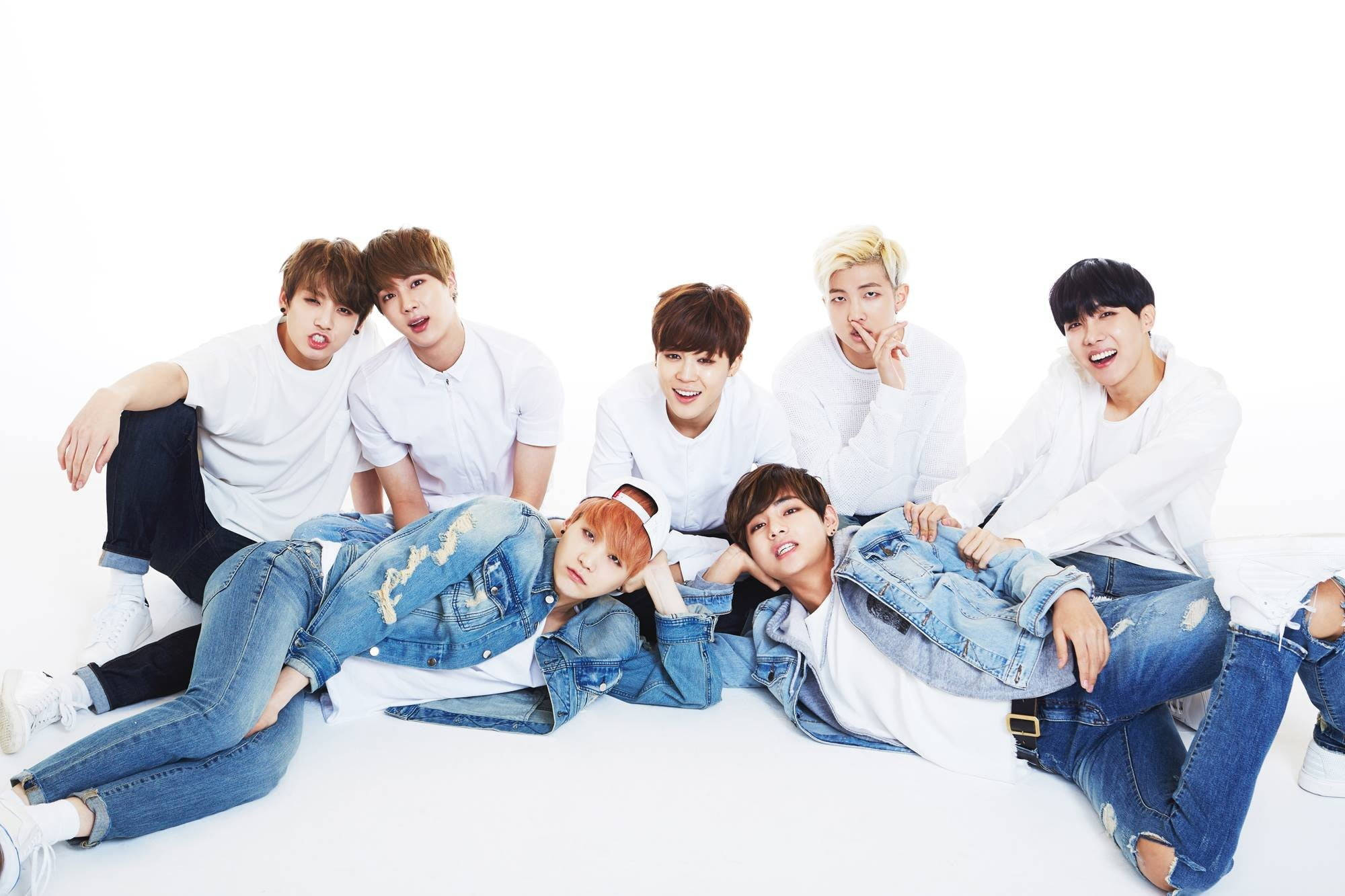 BTS 桌布 壁紙 — 七位身穿白色T恤和牛仔褲的年輕男性在純白背景前俏皮地擺姿勢。