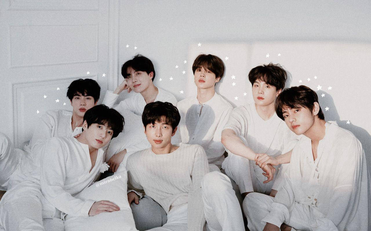 BTS 桌布 壁紙 — 七位身穿白色休閒服的年輕男子在床上一起擺姿勢，周圍有柔和星光效果閃爍。
