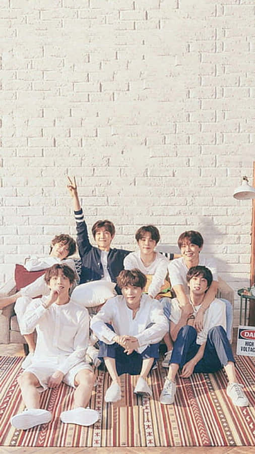 BTS 桌布 壁紙 — 七位身穿白色休閒服裝的年輕男性在白色磚牆前的條紋地毯上愉快地擺姿勢。