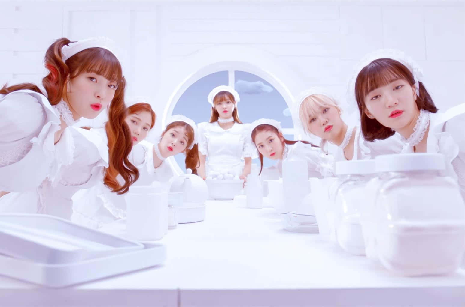 The Idol 桌布 壁紙 — 七位身穿白色女僕裝的年輕女性，在一個明亮簡約的房間裡，圍繞著一張放滿白色容器的白色桌子，擺出俏皮的表情。