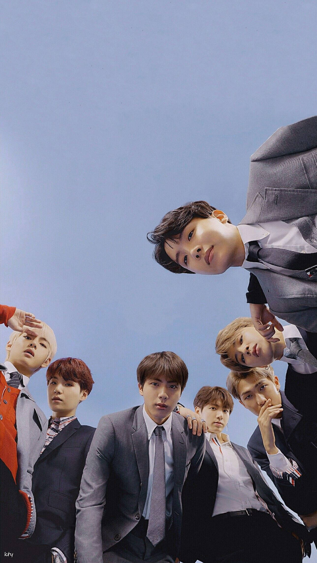 BTS 桌布 壁紙 — 七位身穿筆挺西裝的年輕男士從上方俯身，以清澈藍天為背景，擺出自信的表情。