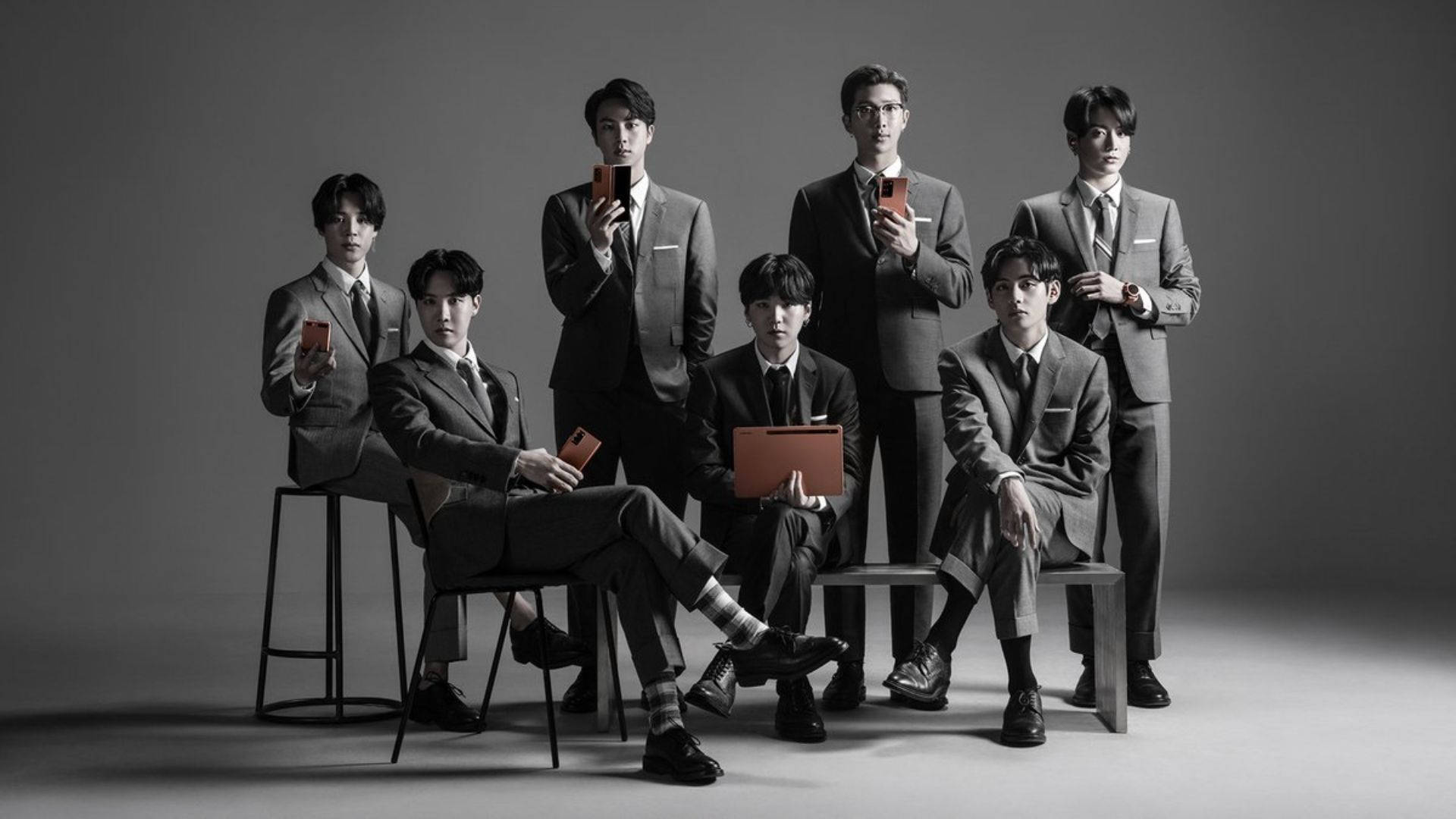 BTS 桌布 桌布 壁紙 — 七位身穿筆挺西裝的男士，在簡約灰色攝影棚背景前，手持橙色電話擺姿勢。