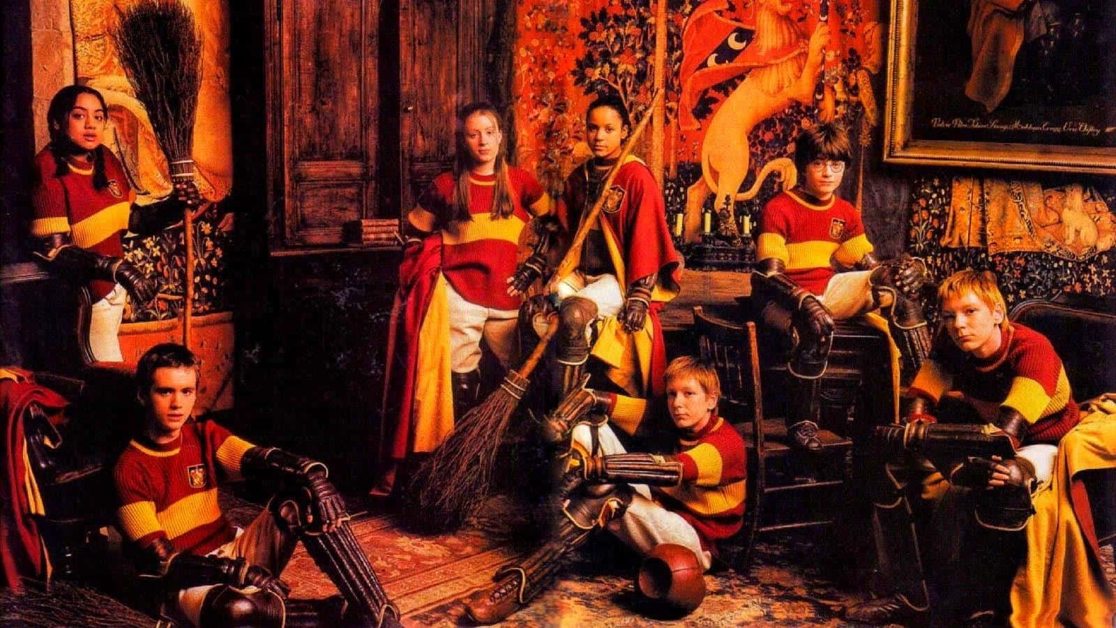 Quidditch 桌布 壁紙 — 七位身穿紅金制服的年輕魁地奇球員在溫暖光線的華麗木房間裡，拿著掃帚擺姿勢。