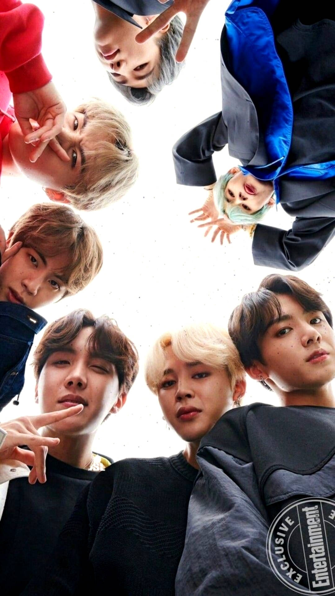 BTS 鎖定螢幕 桌布 壁紙 — 七位身穿色彩繽紛休閒服的年輕男子，在明亮的白色背景前，以俏皮的表情向下看著鏡頭。