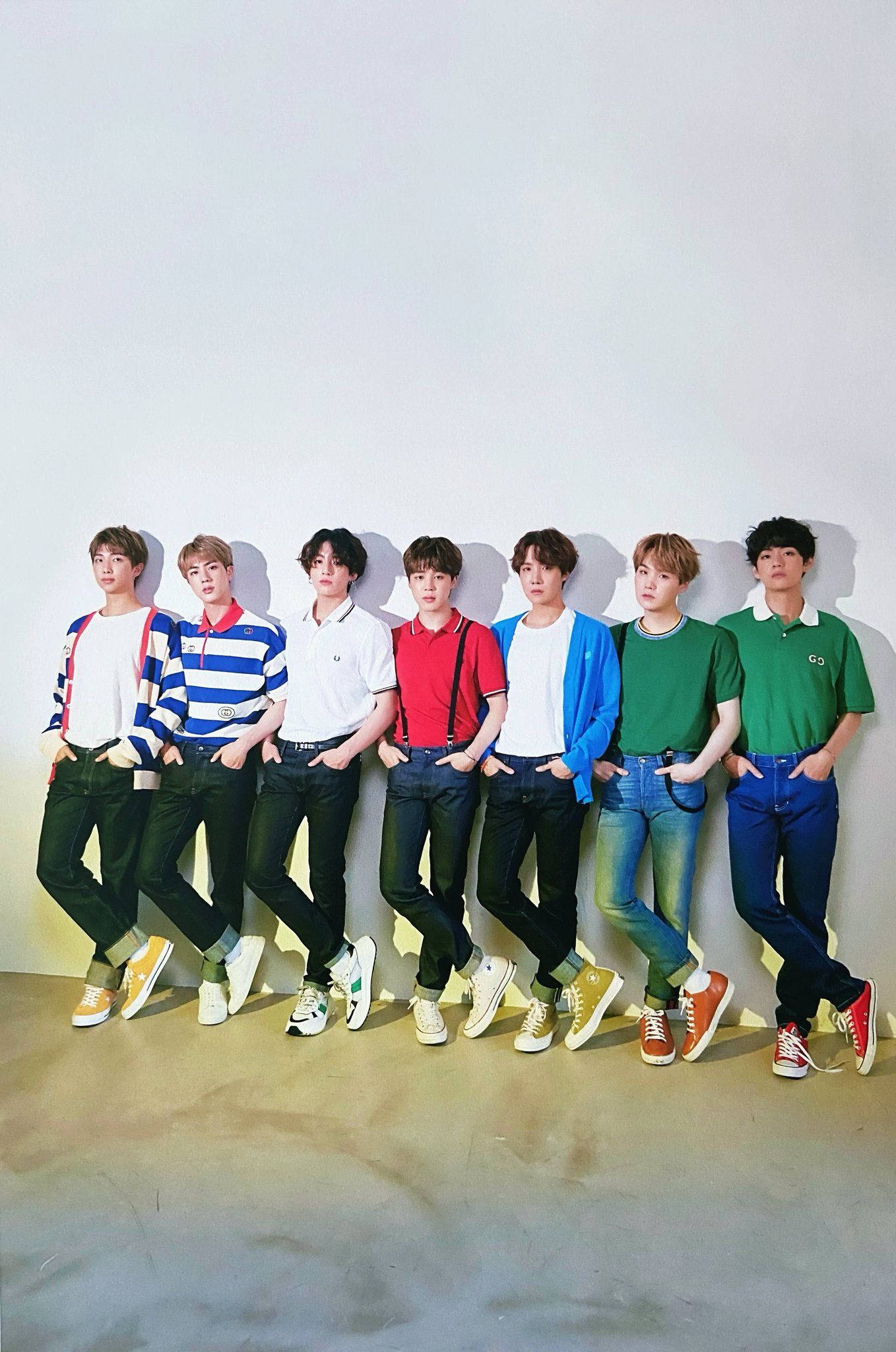 BTS 鎖定螢幕 桌布 壁紙 — 七位身穿色彩繽紛休閒服裝的年輕男子靠在一面素牆上，在混凝土地面投下柔和陰影。