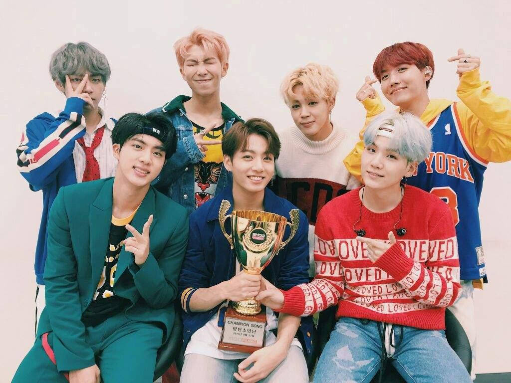 BTS 桌布 桌布 壁紙 — 七位身穿色彩繽紛休閒服裝的年輕男性，在純白背景前開心地拿著金色獎盃擺姿勢。