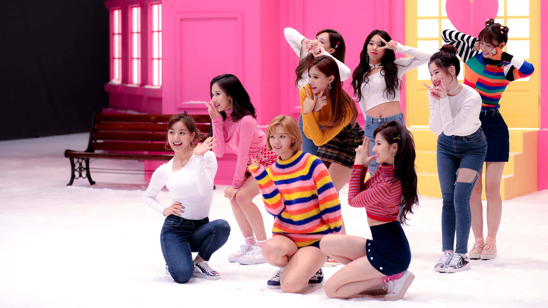 twice 桌布 壁紙 — 七位身穿色彩繽紛服裝的年輕女性，在一個設有木凳的亮粉紅色和黃色場景中俏皮地擺姿勢。