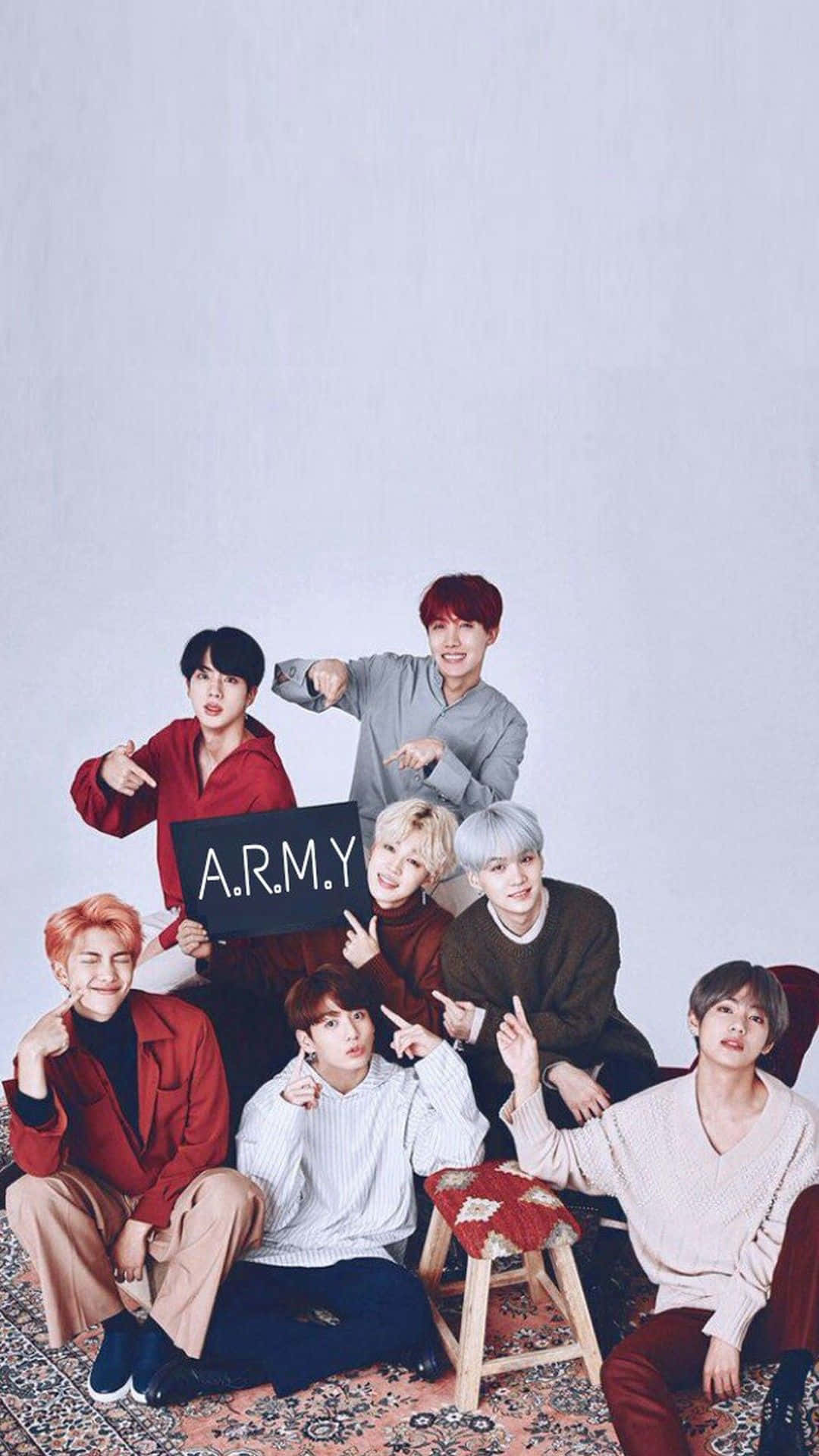 BTS 桌布 壁紙 — 七位身穿色彩繽紛服裝的年輕男子在圖案地毯上俏皮地擺姿勢，手持寫著A.R.M.Y.的牌子。