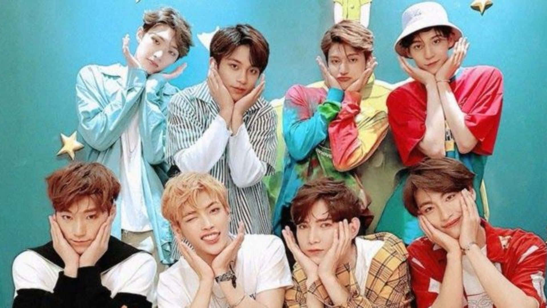 Ateez Desktop 桌布 壁紙 — 七位身穿色彩繽紛服裝的年輕男性，在帶有金色星星的藍綠色背景前，將手放在臉頰上俏皮地擺姿勢。
