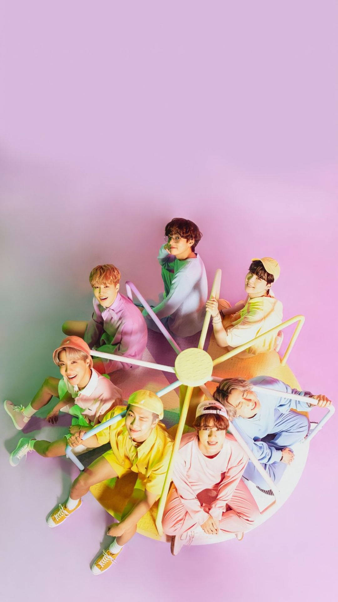 BTS 桌布 壁紙 — 七位身穿色彩繽紛粉彩服裝的年輕男子，在柔和的紫色背景下，於黃色摩天輪上愉快地擺姿勢。