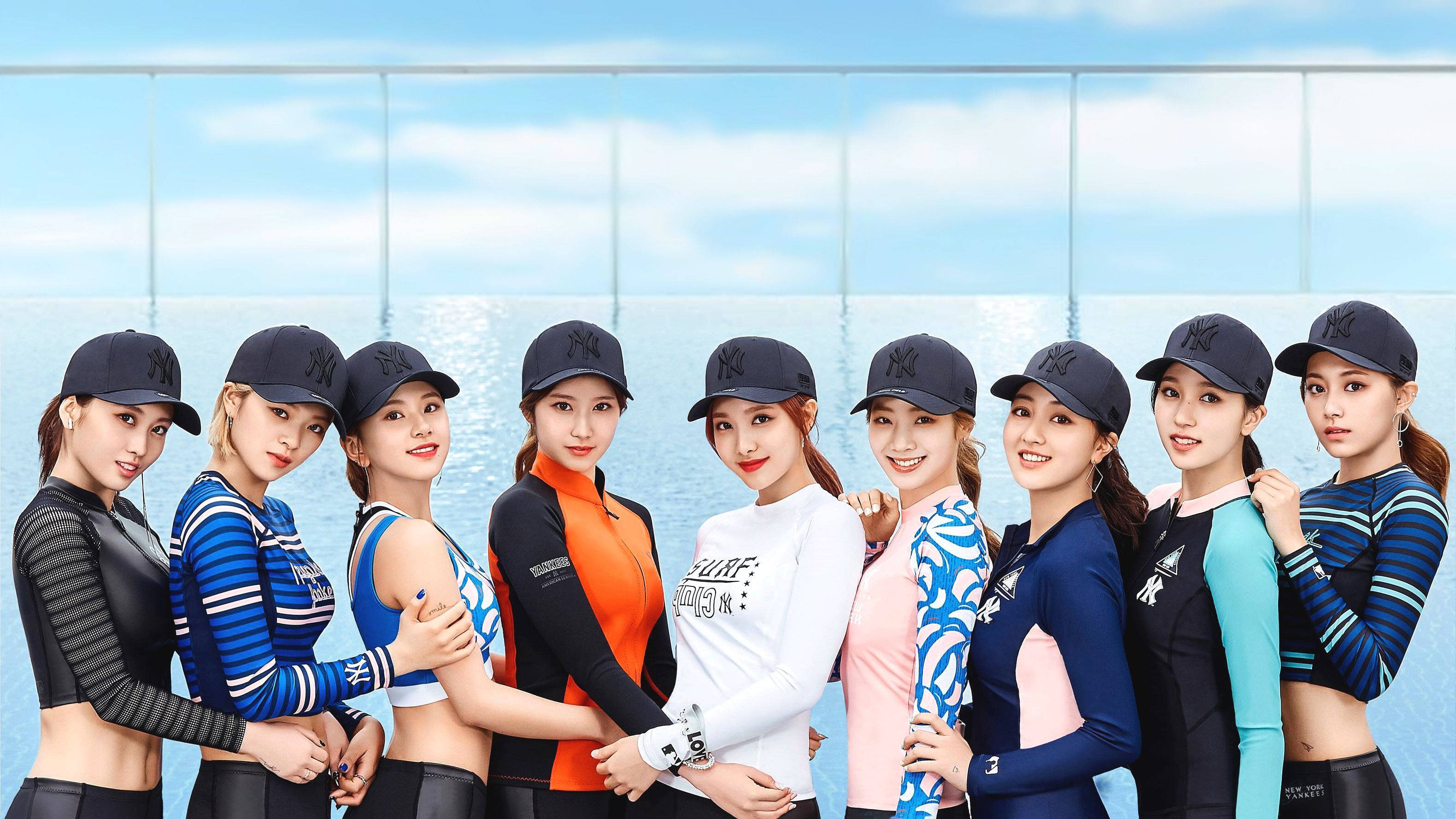 twice 桌布 壁紙 — 七位身穿運動服和帽子的女性在明亮的藍天和玻璃牆背景下自信地擺姿勢。