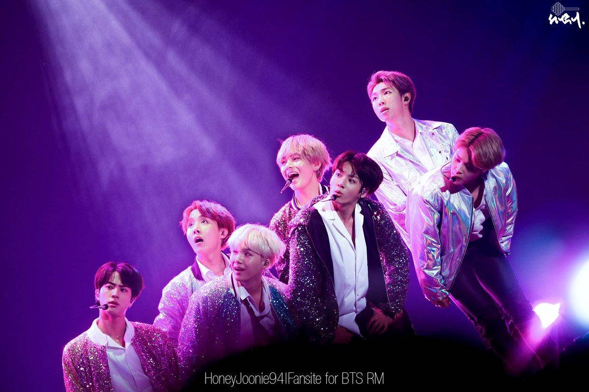 BTS 桌布 壁紙 — 七位身穿閃亮外套的男表演者在戲劇性的紫色舞台燈光下擺出動感姿勢。