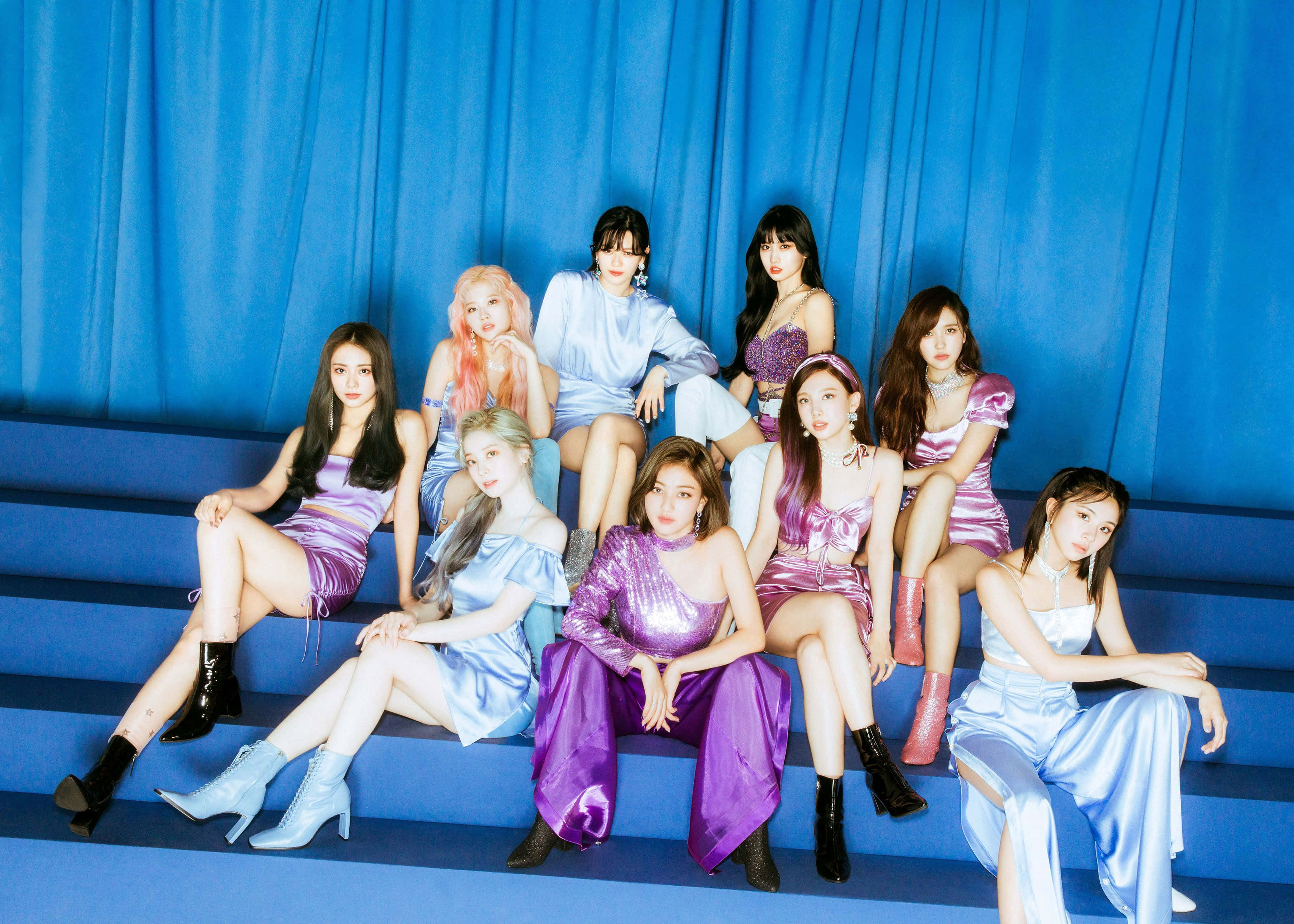 K-pop 桌布 壁紙 — 七位身穿閃亮紫色和藍色服裝的女性在藍色台階上自信地擺姿勢，背景是相配的窗簾。