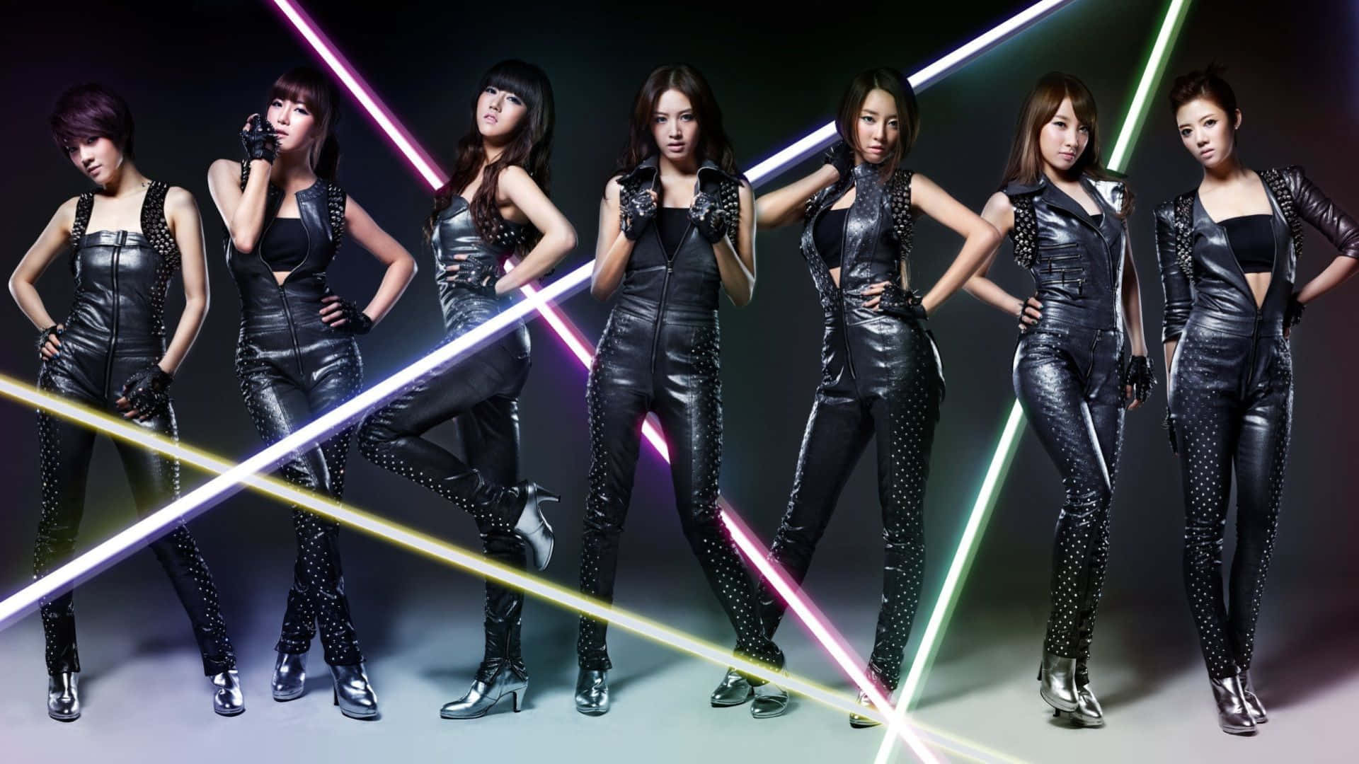 K-pop 桌布 壁紙 — 七位身穿閃亮黑色皮革服裝的女性，在色彩繽紛的霓虹雷射光束照射的黑暗背景下自信地擺姿勢。
