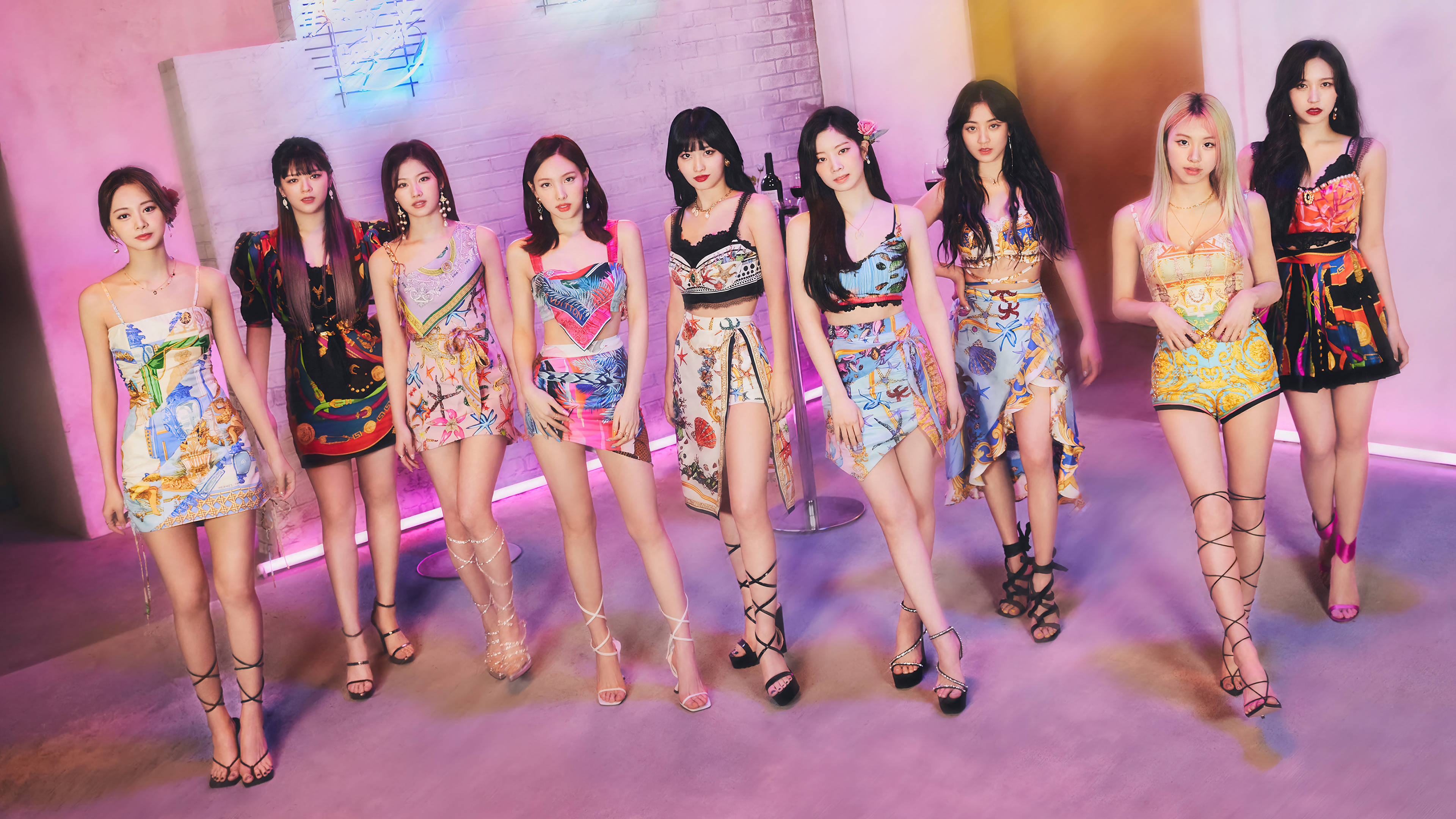 Kpop Aesthetic 桌布 壁紙 — 七位身穿鮮豔圖案服裝的女性在粉紅色霓虹燈下，於風格化的攝影棚中自信地擺出姿勢。