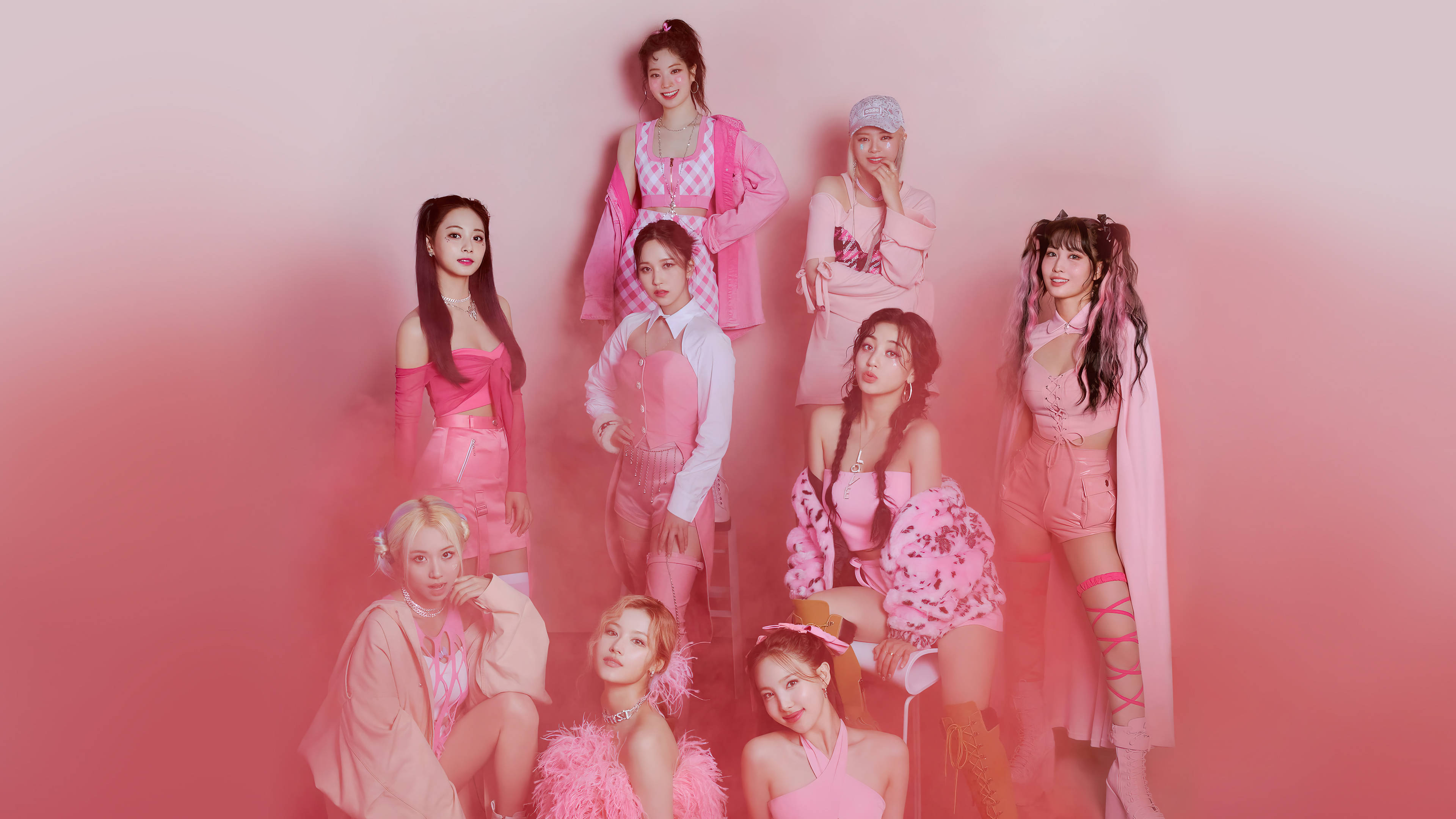 Kpop Aesthetic 桌布 壁紙 — 七位身穿鮮豔粉紅色服裝的女性在攝影棚中，自信地擺出姿勢，背景是柔和的漸變粉紅色。