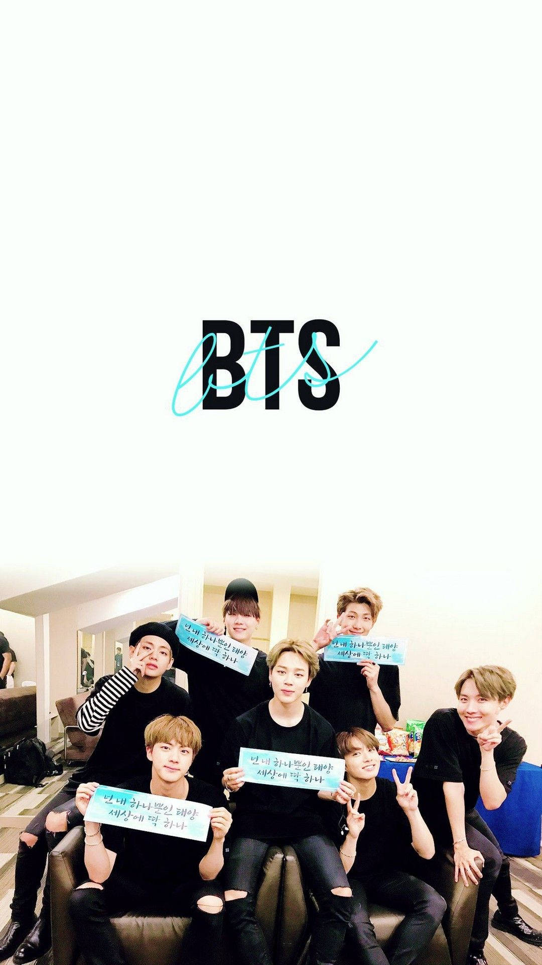 BTS 2021 桌布 壁紙 — 七位身穿黑色服裝的年輕男子在白色背景前，於一個大型BTS標誌下，手持韓文標語牌，在沙發上愉快地擺姿勢。