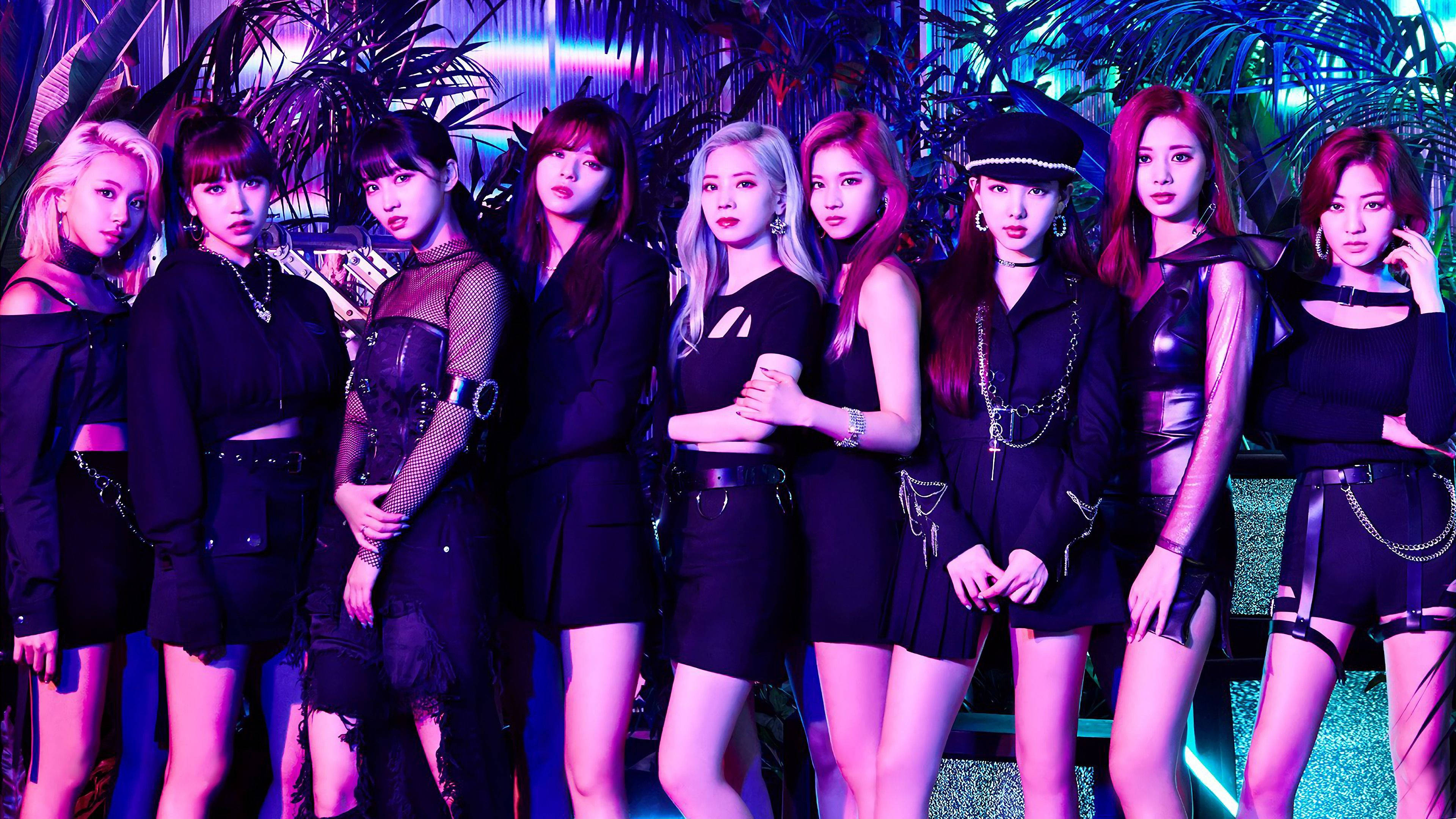 Kpop Aesthetic 桌布 壁紙 — 七位身穿黑色服裝的時尚女性在熱帶植物中，於霓虹紫色和藍色燈光下自信地擺姿勢。