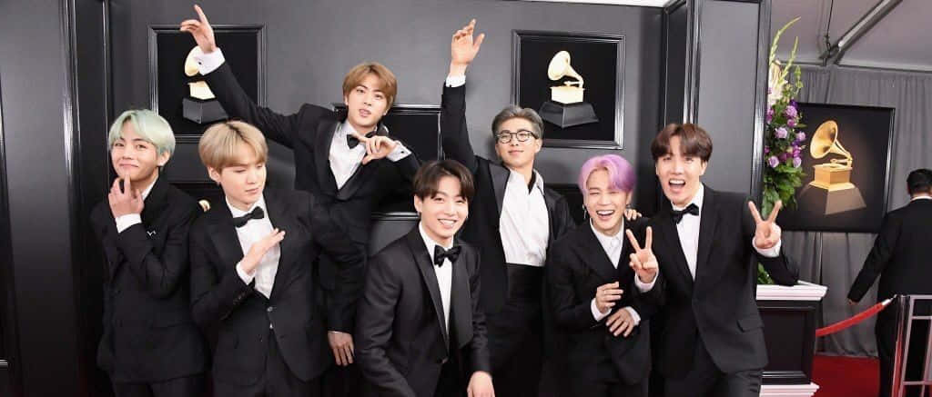 Big Hit Entertainment 桌布 壁紙 — 七位身穿黑色燕尾服、頭髮色彩繽紛的男士在紅地毯上與葛萊美獎盃旁愉快地擺姿勢。