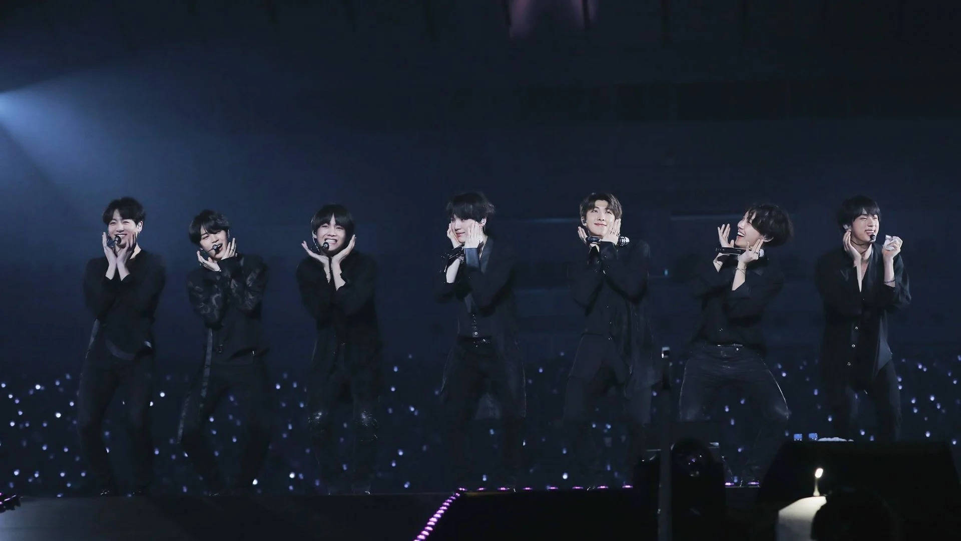 BTS 桌布 壁紙 — 七位身穿黑色西裝的男表演者在藍色舞台燈光及閃爍地板效果下熱情演唱。