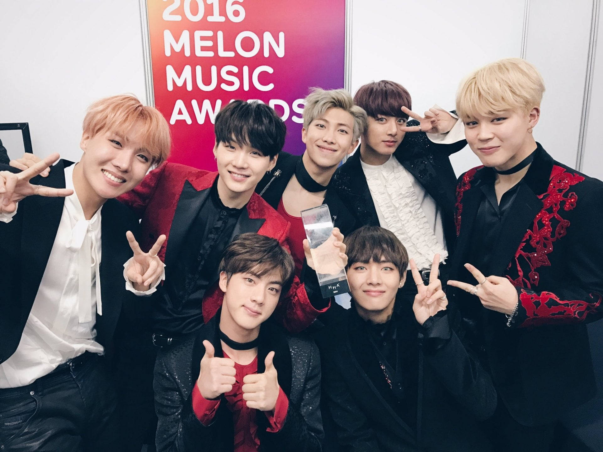 桌布 壁紙 — 七位面帶微笑的K-pop偶像身穿黑色和紅色服裝，在2016年Melon Music Awards上手持獎盃擺姿勢。