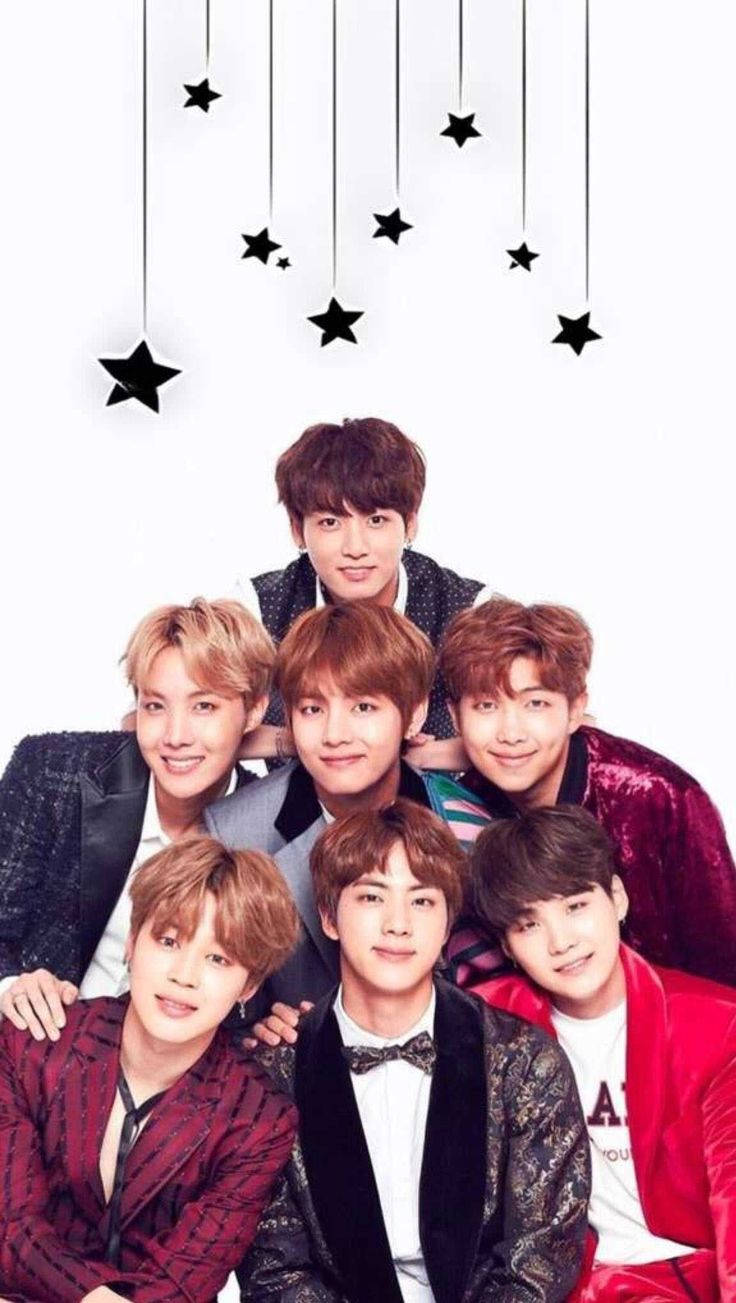 BTS 桌布 壁紙 — 七位面帶微笑的年輕男士身著時尚西裝，在白色背景懸掛的黑色星星下一起擺姿勢。