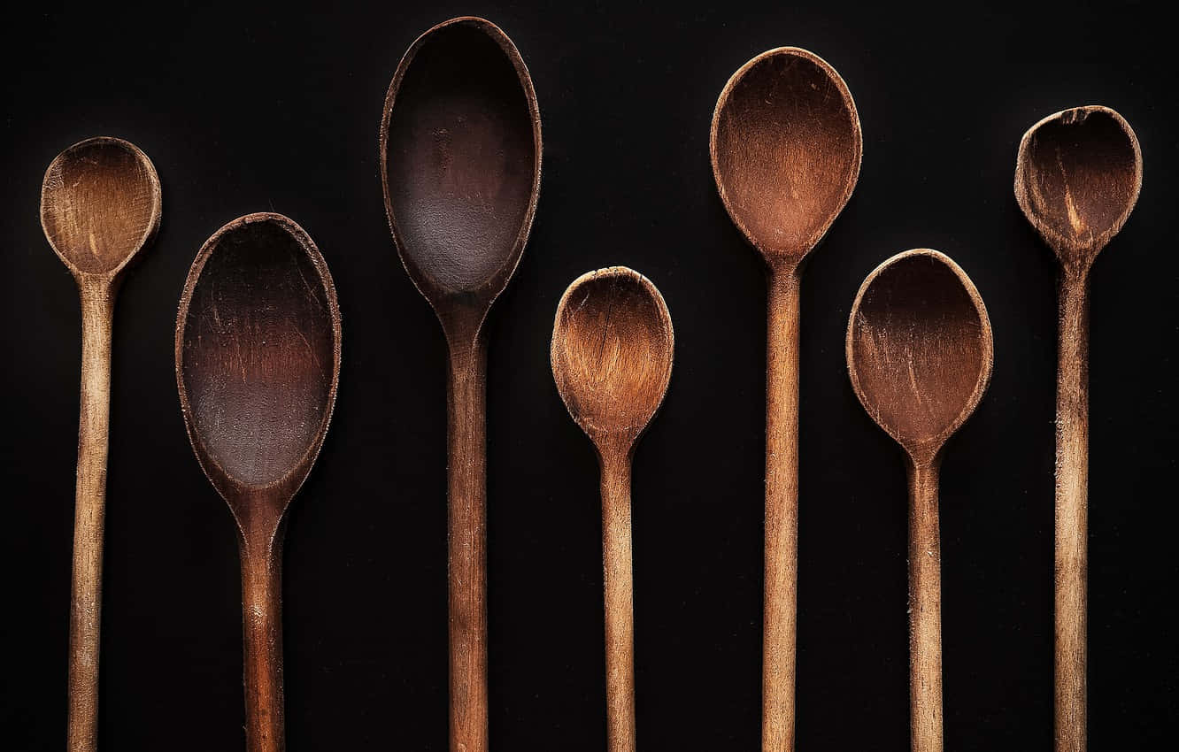 Wooden Spoon 桌布 壁紙 — 七個不同尺寸的鄉村風格木勺在純黑背景上排成一排。