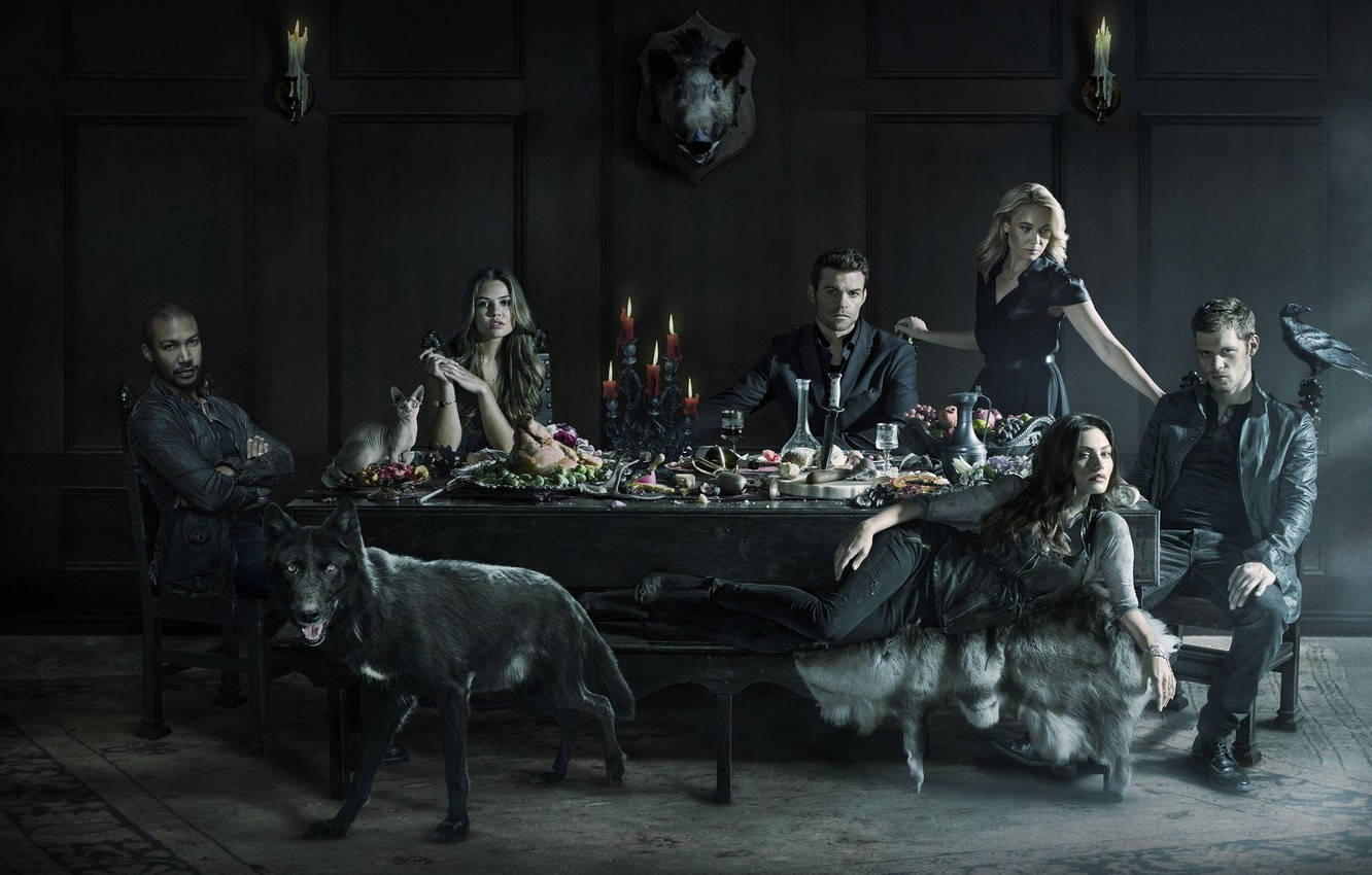 elijah mikaelson 桌布 壁紙 — 七個人和一隻狼圍繞著一張燭光晚餐桌，在一個黑暗的哥德式房間裡，房間裡有一個安裝好的熊頭。