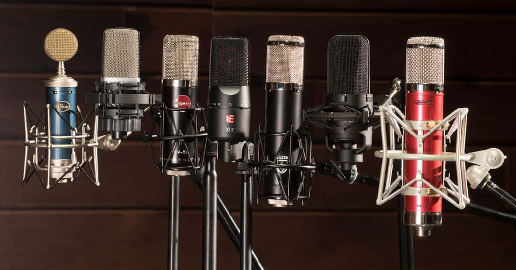 Microphones 桌布 壁紙 — 七個專業錄音室麥克風，顏色和設計各異，一字排開，背景為深色木質。
