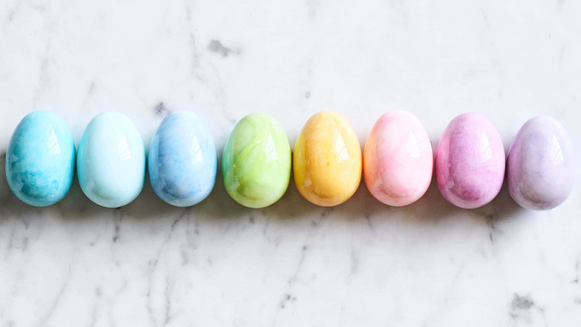 Easter Zoom 桌布 壁紙 — 七個帶有大理石紋理的柔和色調復活節蛋整齊地排列在白色大理石表面上。