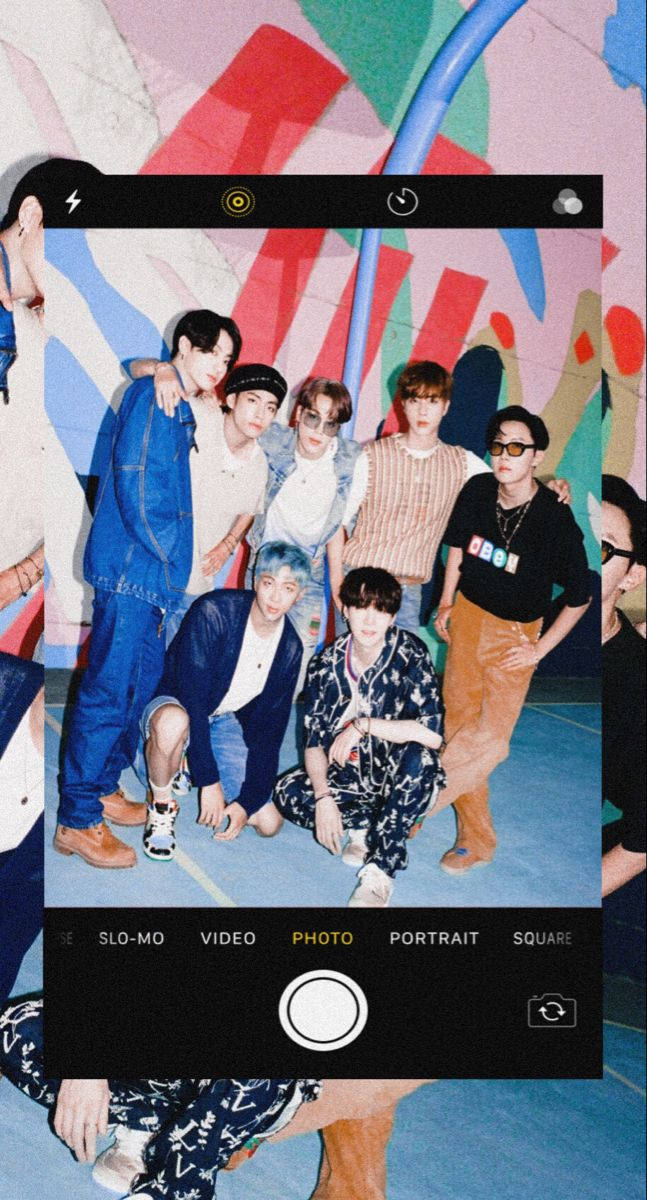bts iPhone 桌布 壁紙 — 七個年輕男子在一個充滿活力的塗鴉房間裡隨意擺姿勢，由智慧型手機相機介面包圍。