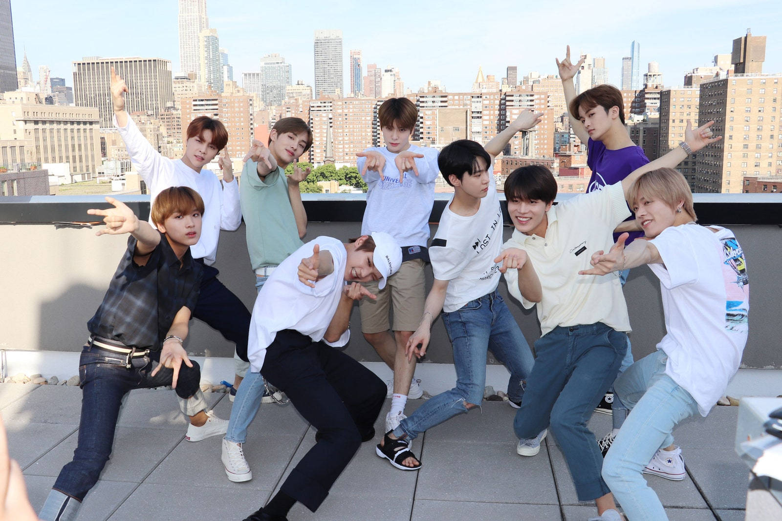 Nct 桌布 壁紙 — 七個年輕男子在屋頂上擺出充滿動感的舞蹈姿勢，背後是廣闊的城市天際線，在明亮的日光下。