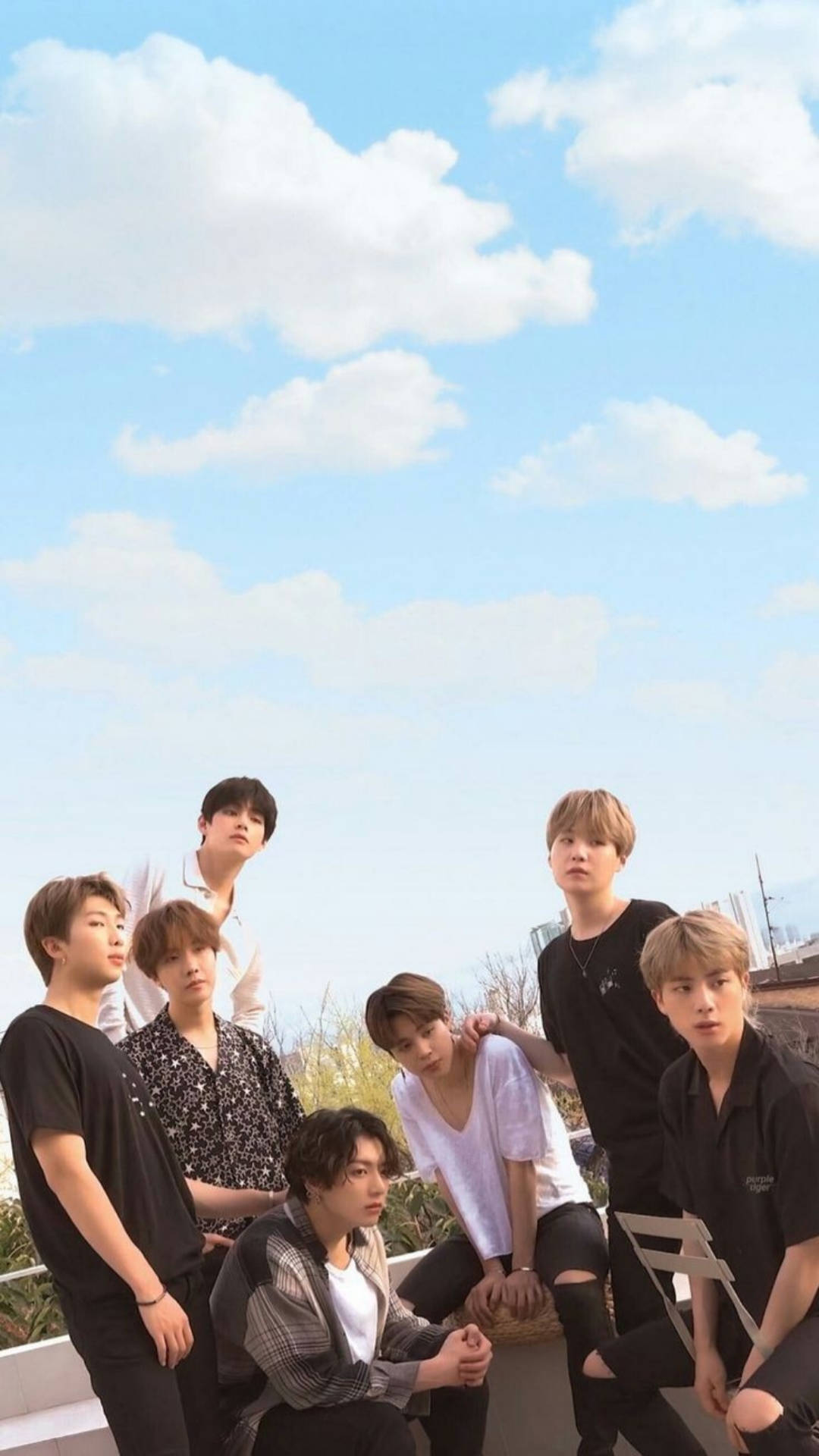BTS 鎖定螢幕 桌布 壁紙 — 七個年輕男子在藍天白雲下的屋頂上隨意擺姿勢。