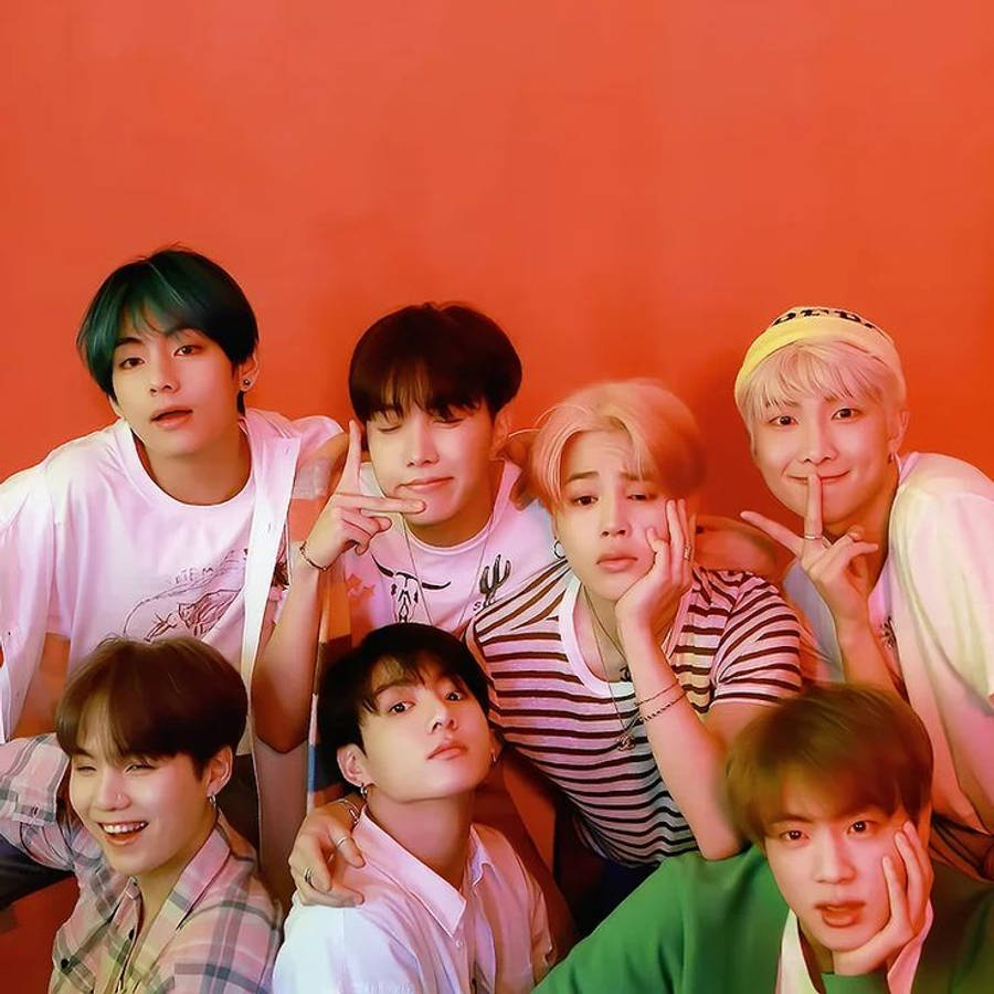 BTS 桌布 壁紙 — 七個年輕男子有色彩繽紛的頭髮，穿著休閒服裝，在純色珊瑚牆前頑皮地擺姿勢。