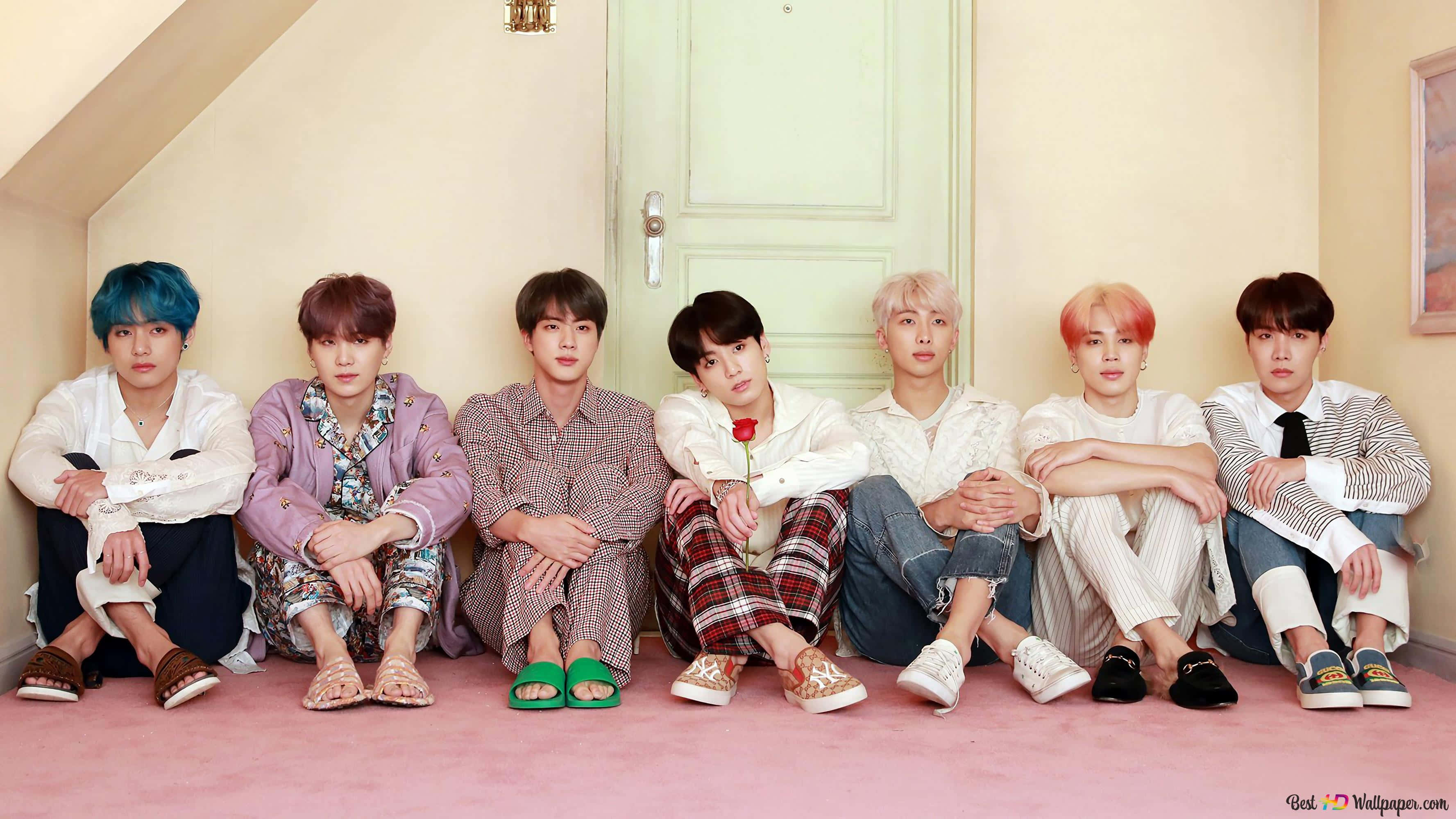 BTS 桌布 壁紙 — 七個年輕男子有色彩繽紛的頭髮，隨意地坐在粉紅色地板上，背景是淺綠色門，在舒適的閣樓房間裡。