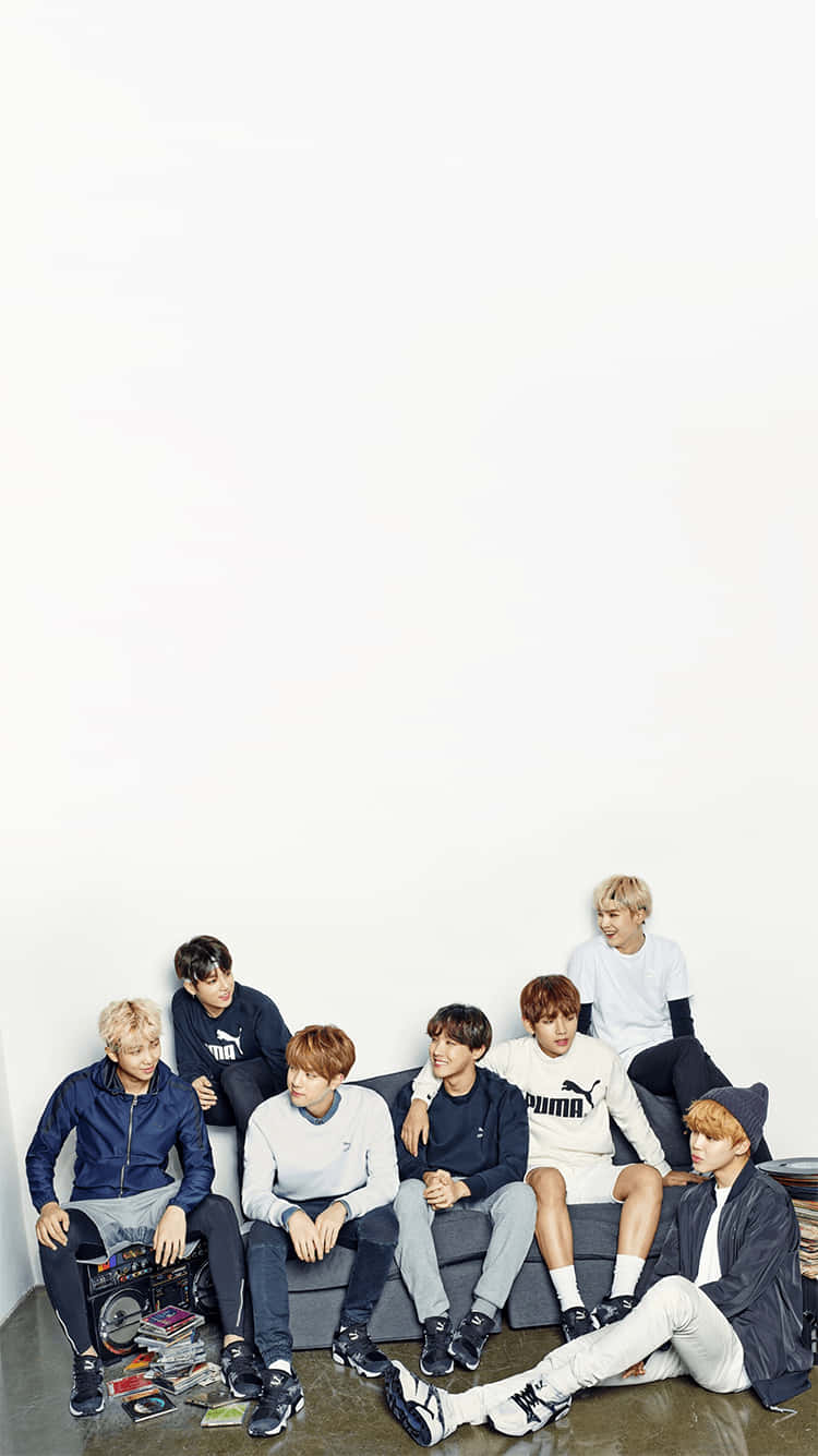 BTS 桌布 壁紙 — 七個年輕男子穿著休閒運動服，靠著白色牆壁，懶散地坐在灰色沙發上，周圍散落著唱片和一部手提音響。