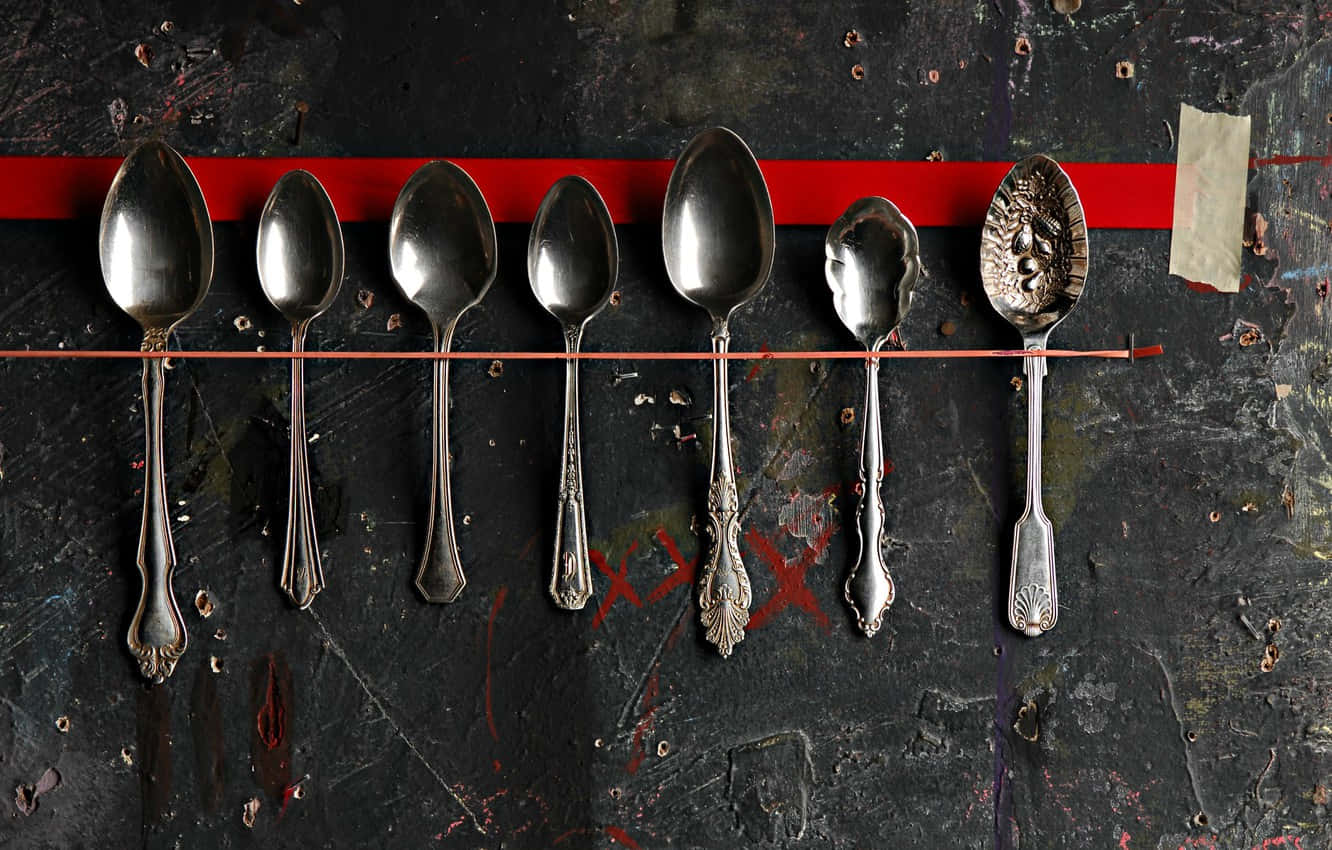 kitchen 桌布 壁紙 — 七個復古銀湯匙掛在一排，背景是粗糙的深色牆壁，上面有搶眼的紅色條紋和塗鴉。