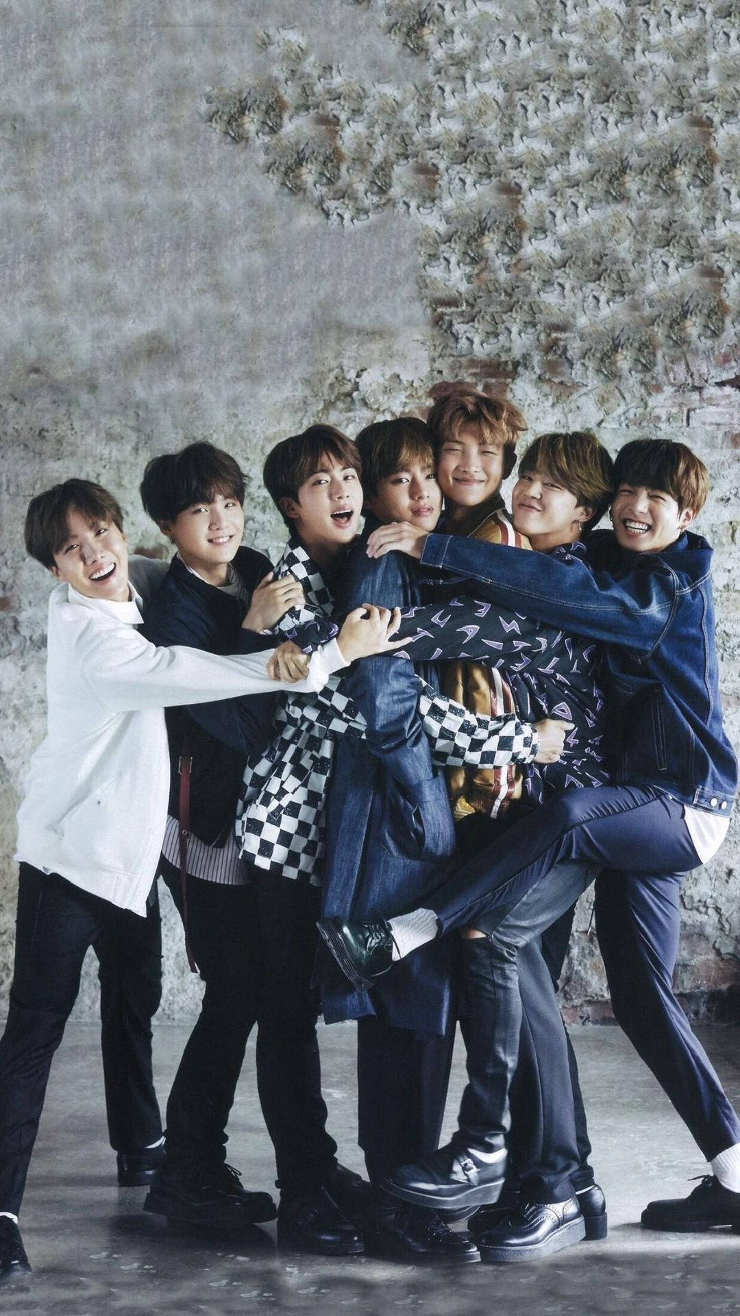 BTS 桌布 壁紙 — 七個微笑的年輕男子穿著休閒服裝，擠在一起靠著紋理混凝土牆。