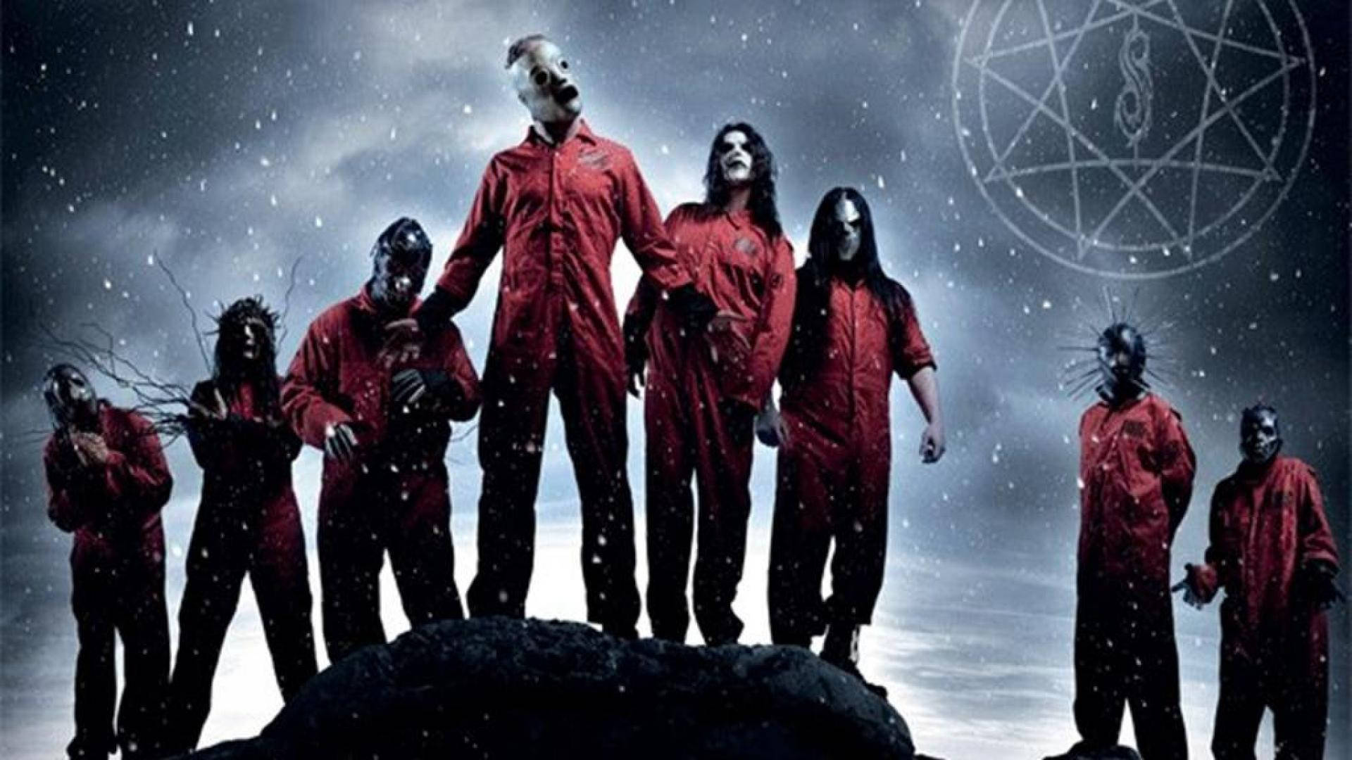 Slipknot 桌布 壁紙 — 七個戴面具、身穿紅色連身衣的人物站在雪覆蓋的岩石上，暴風雨的天空下，上方有一個發光的五角星。