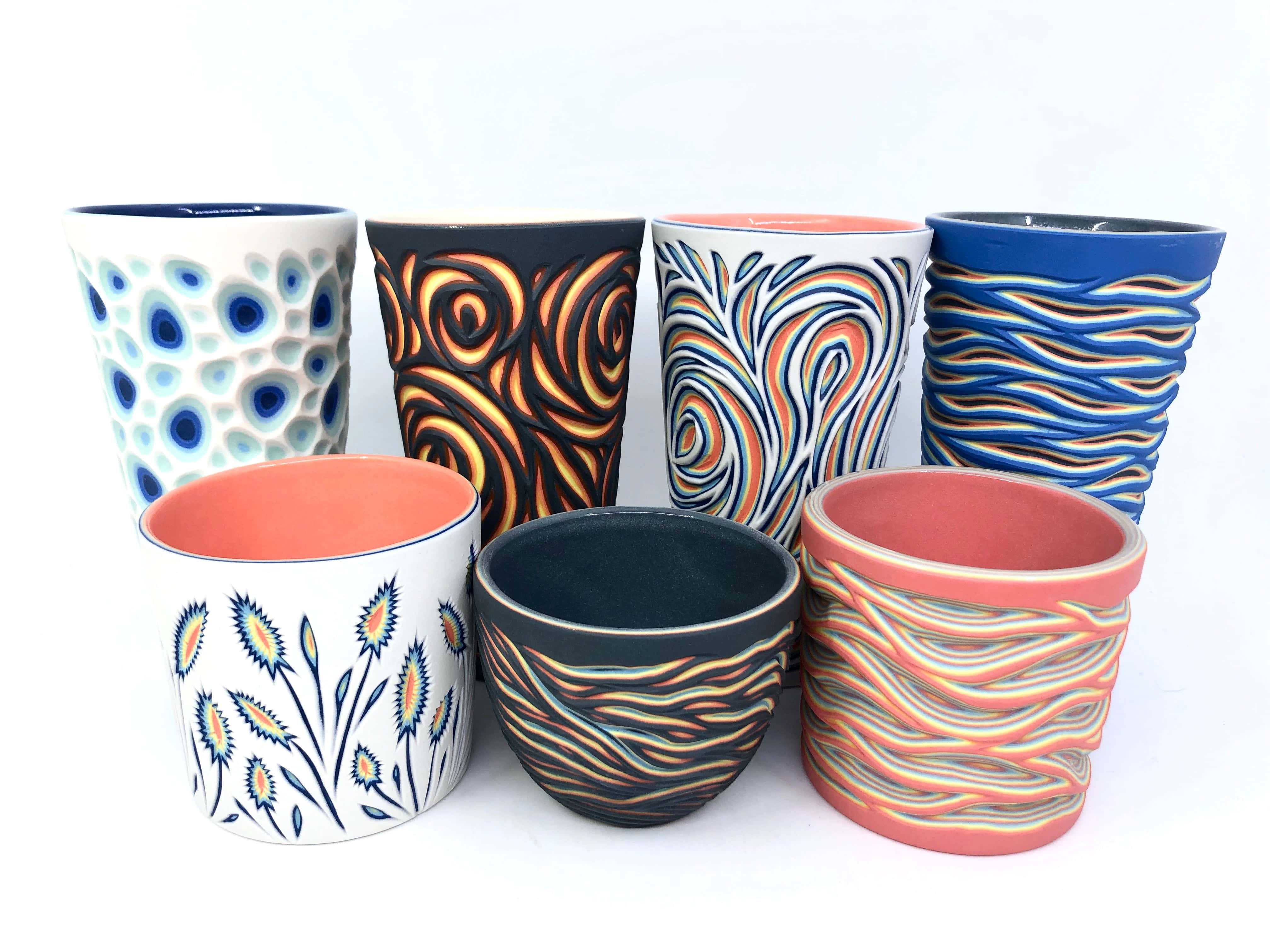 Ceramic 桌布 壁紙 — 七個手工製作的陶瓷馬克杯，帶有鮮豔大膽的圖案，包括漩渦、波浪和花卉圖案，排列在潔白的背景上。